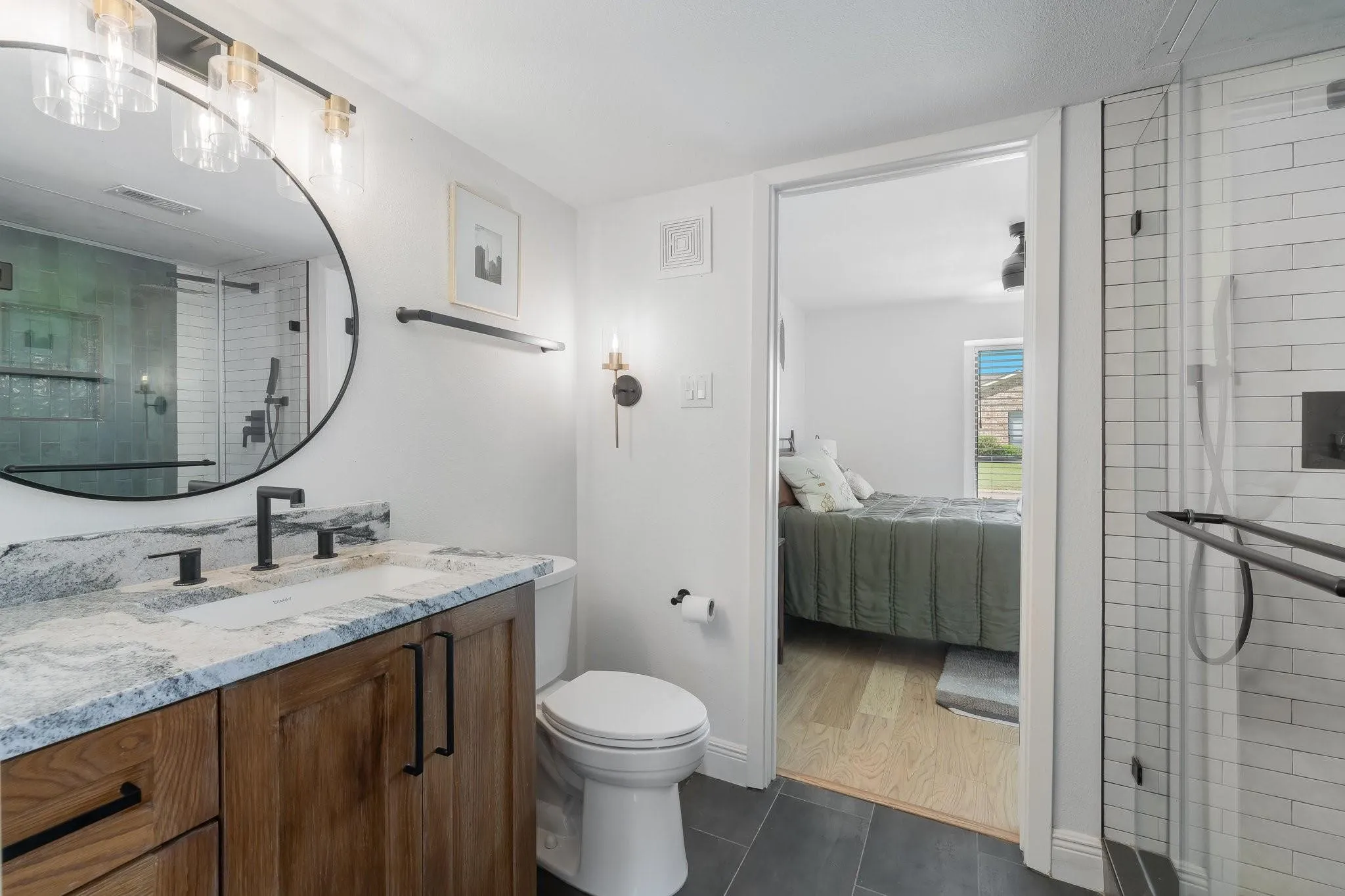 Bathroom featuring a wood-finish vanity with dual sinks, a large round mirror, and a walk-in shower with subway tile