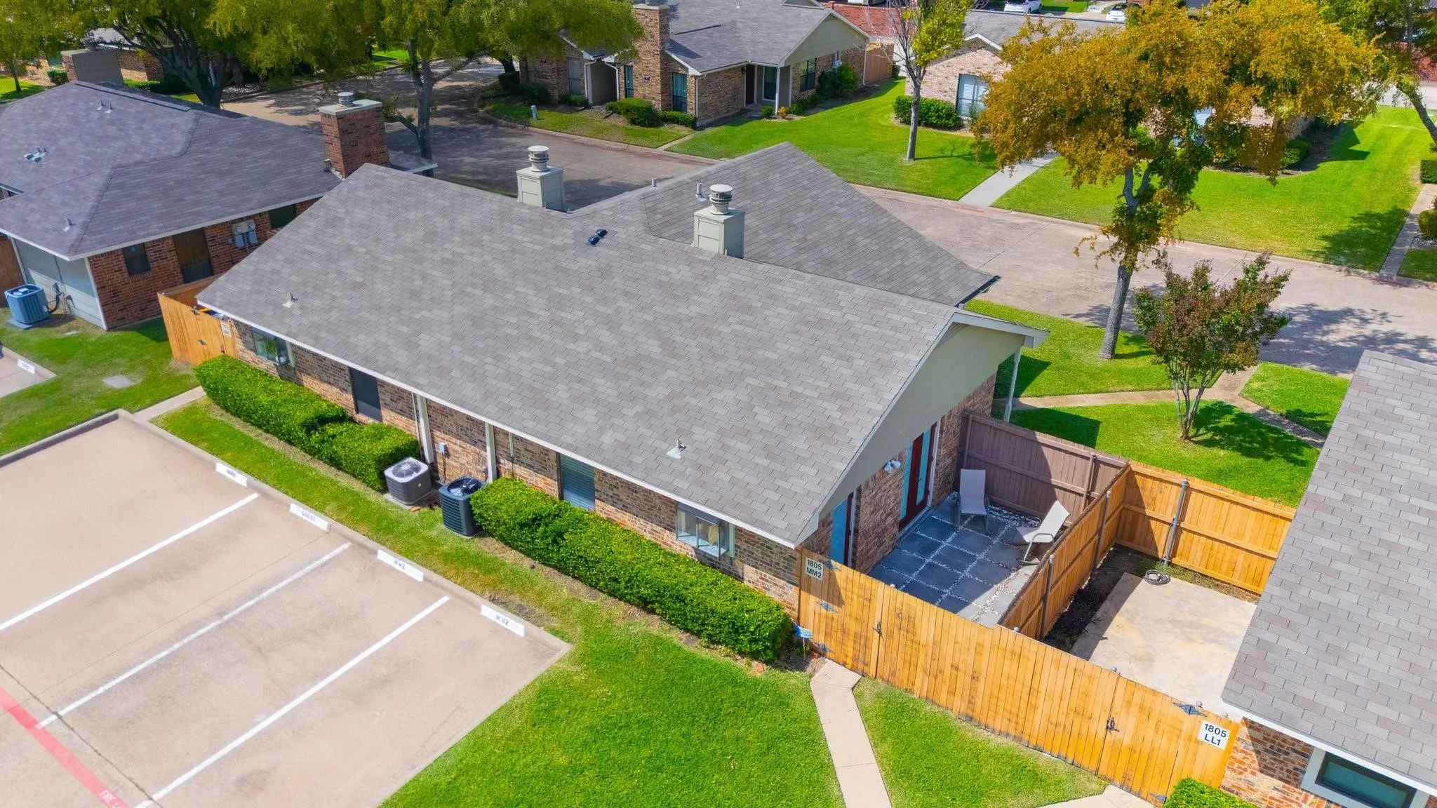 Brick exterior with a gray shingled roof, featuring a fenced private patio with paving stones