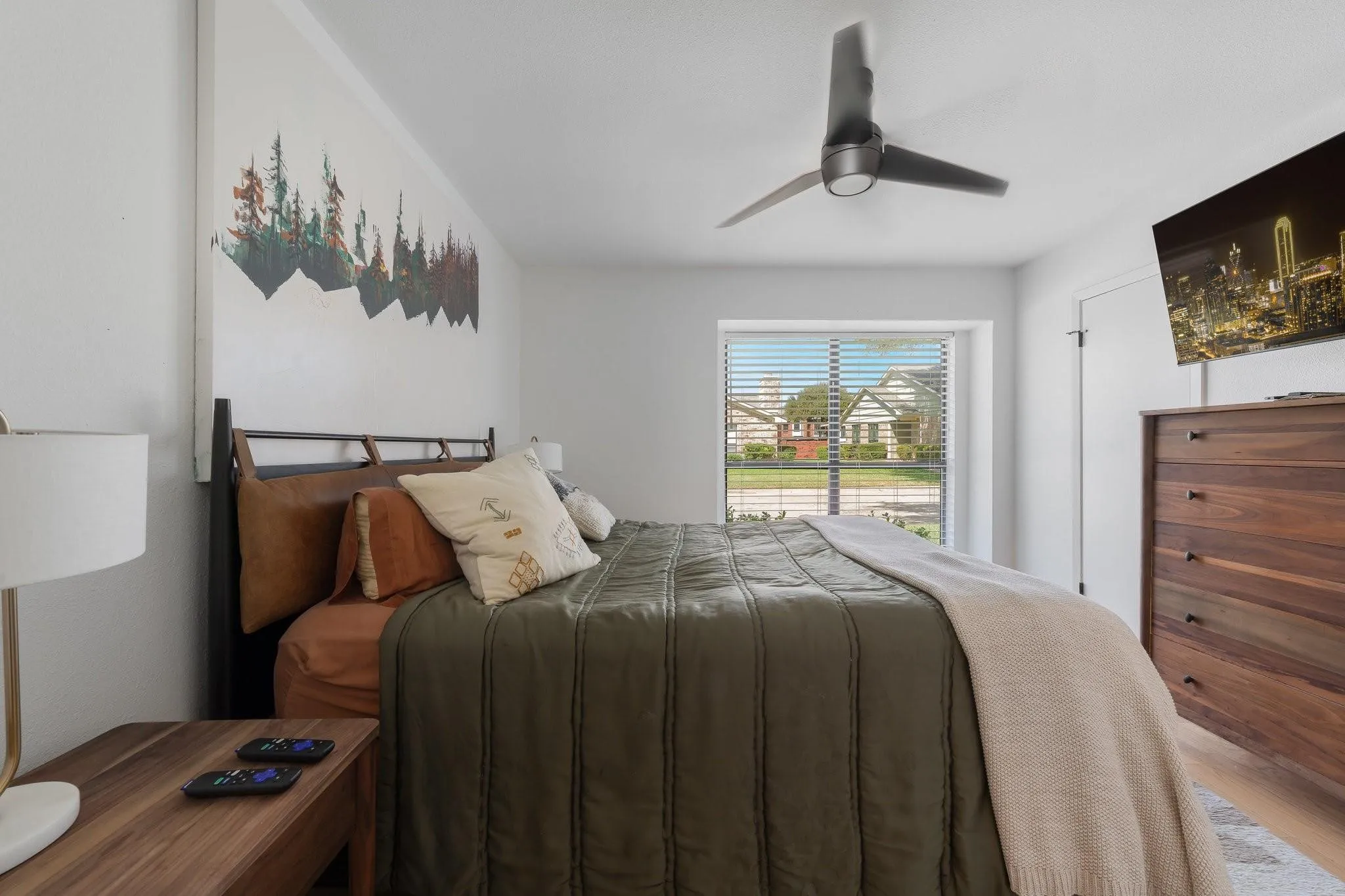 Bright bedroom featuring a large window with horizontal blinds, a ceiling fan, and wood-finish flooring