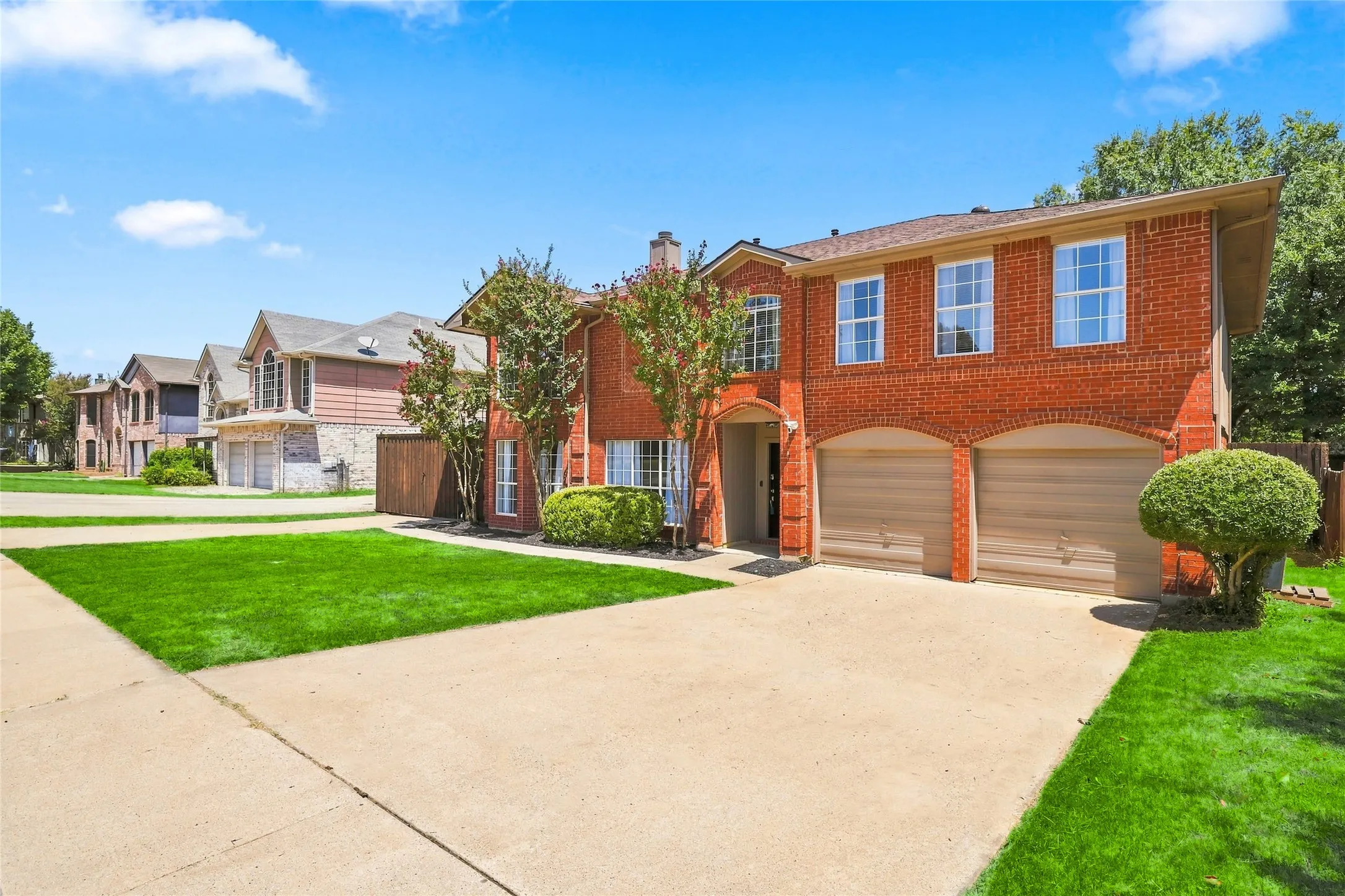 Red brick exterior with arched garage doors, two-car garage, concrete driveway, and front lawn