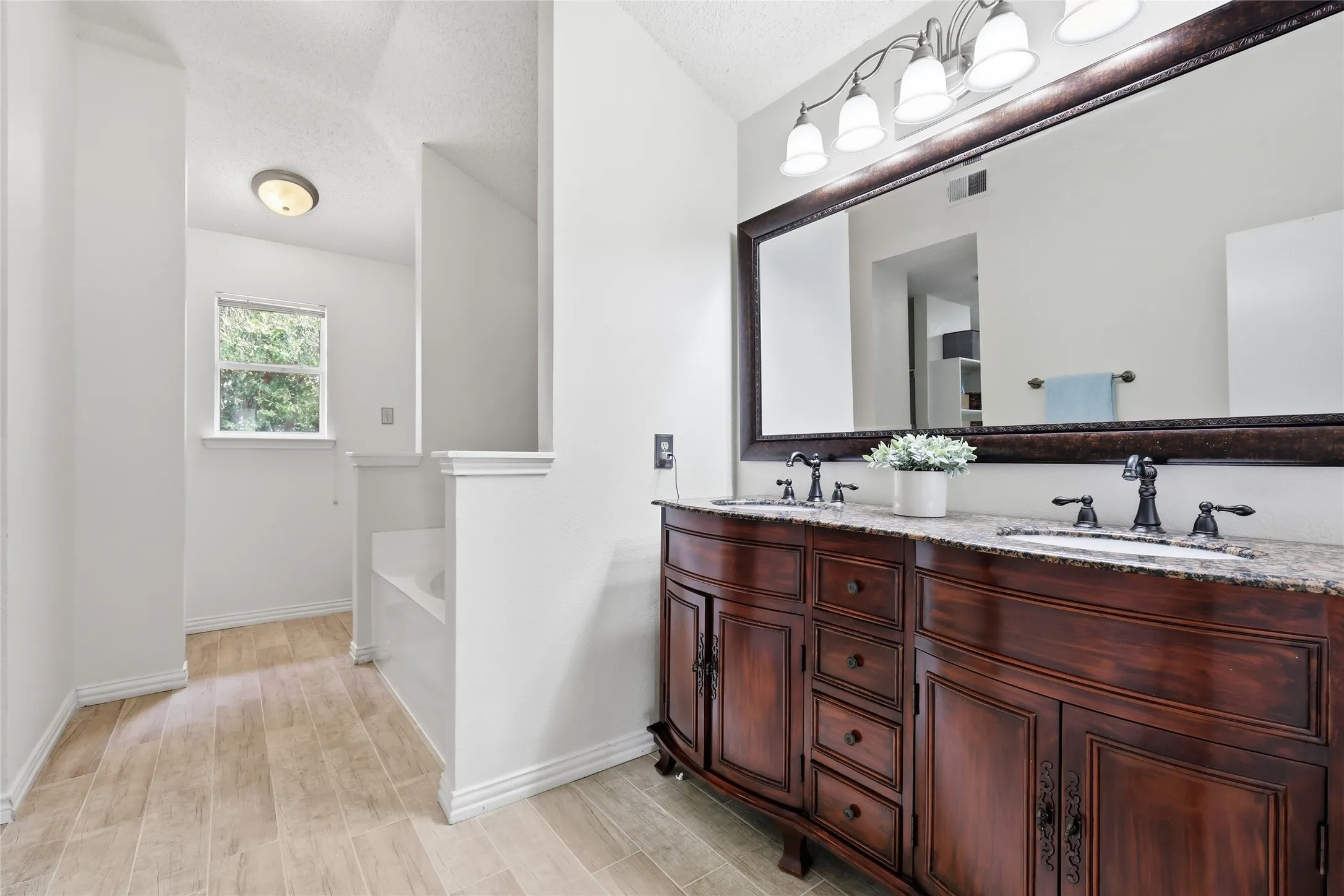 Dual vanity with rich wood-finish cabinetry, integrated sinks, and a large framed mirror