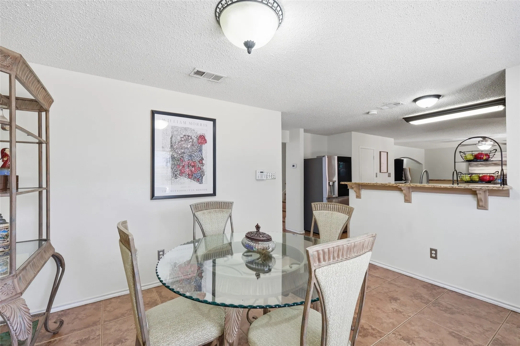 Tile flooring, ceiling-mounted light fixture, breakfast bar with wood-finish shelving, and kitchen pass-through