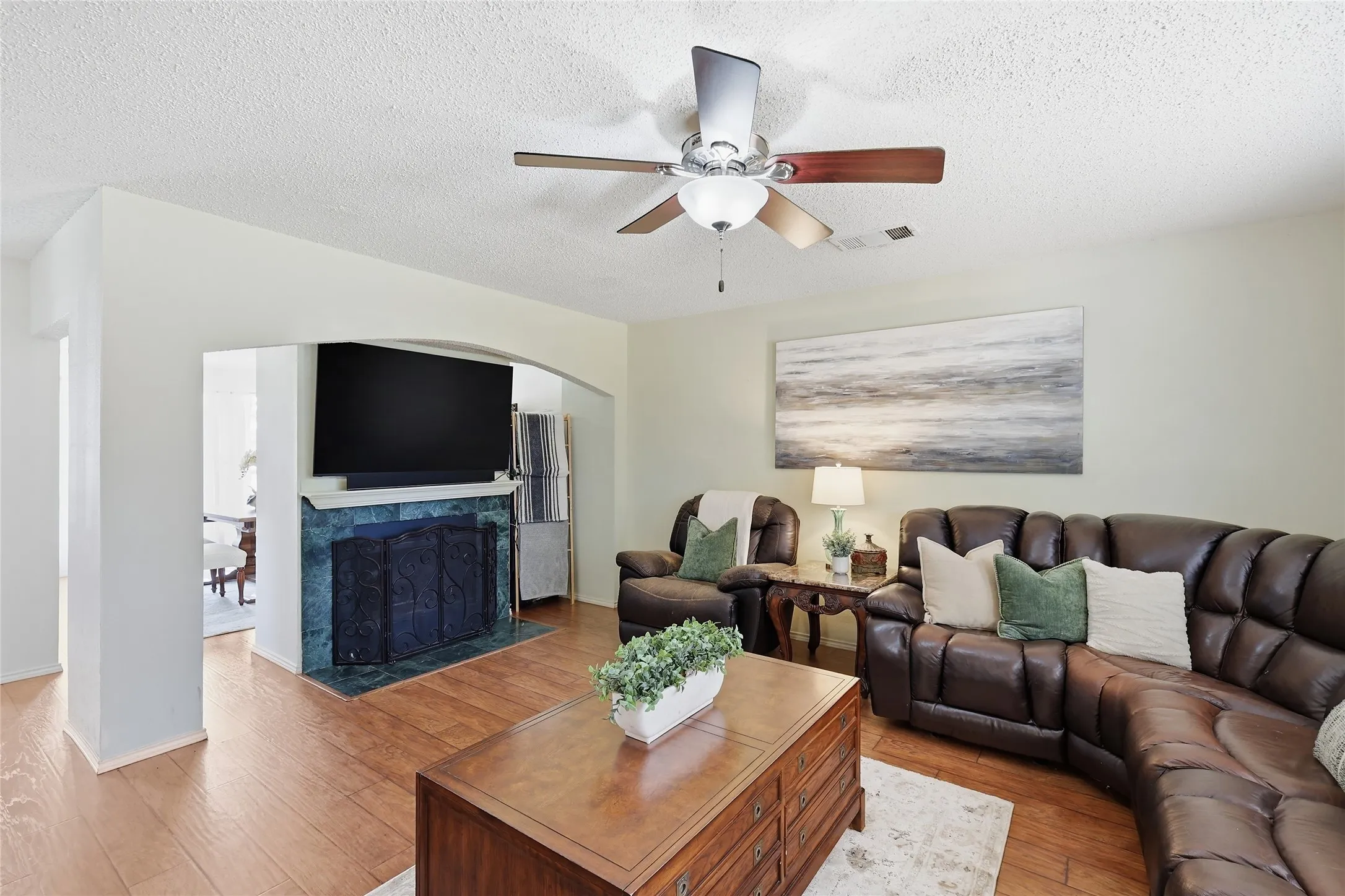 Wood-finish flooring throughout, a ceiling fan with integrated lighting, and a fireplace with a stone surround