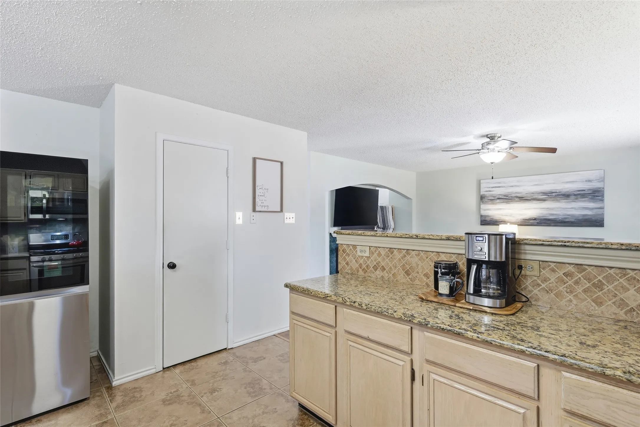 Kitchen featuring light wood cabinetry, stone countertops, stone tile backsplash, and tile flooring