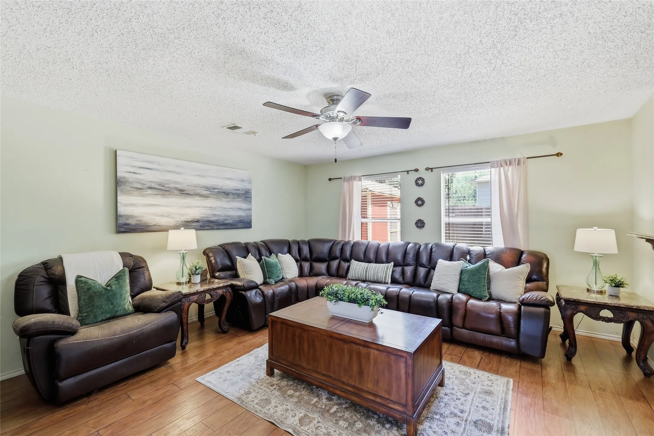 Living area featuring wood-finish flooring, a ceiling fan with integrated lighting, and multiple windows with blinds