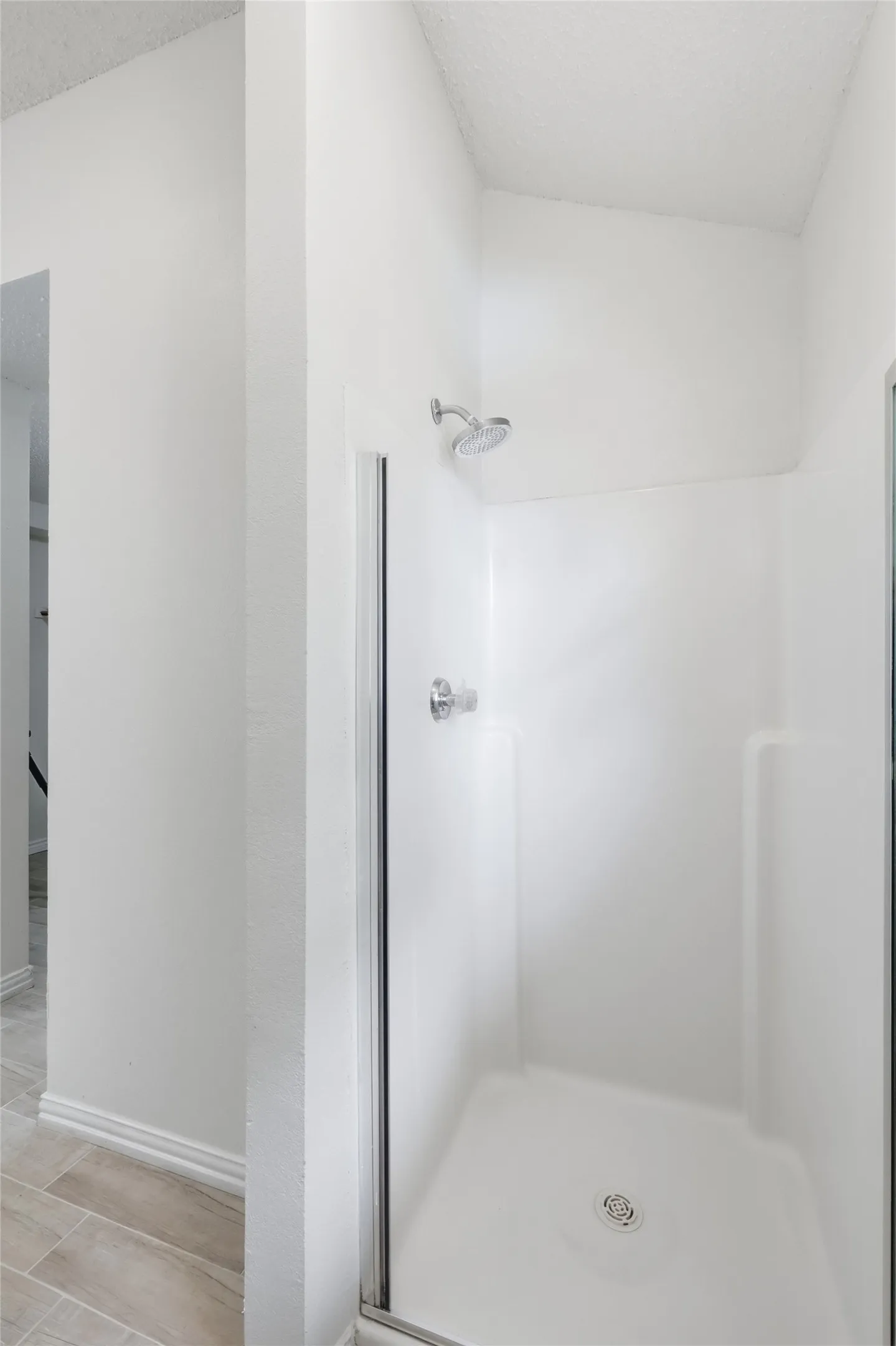 Shower with a clear glass enclosure, a chrome showerhead, and a white integrated shower base