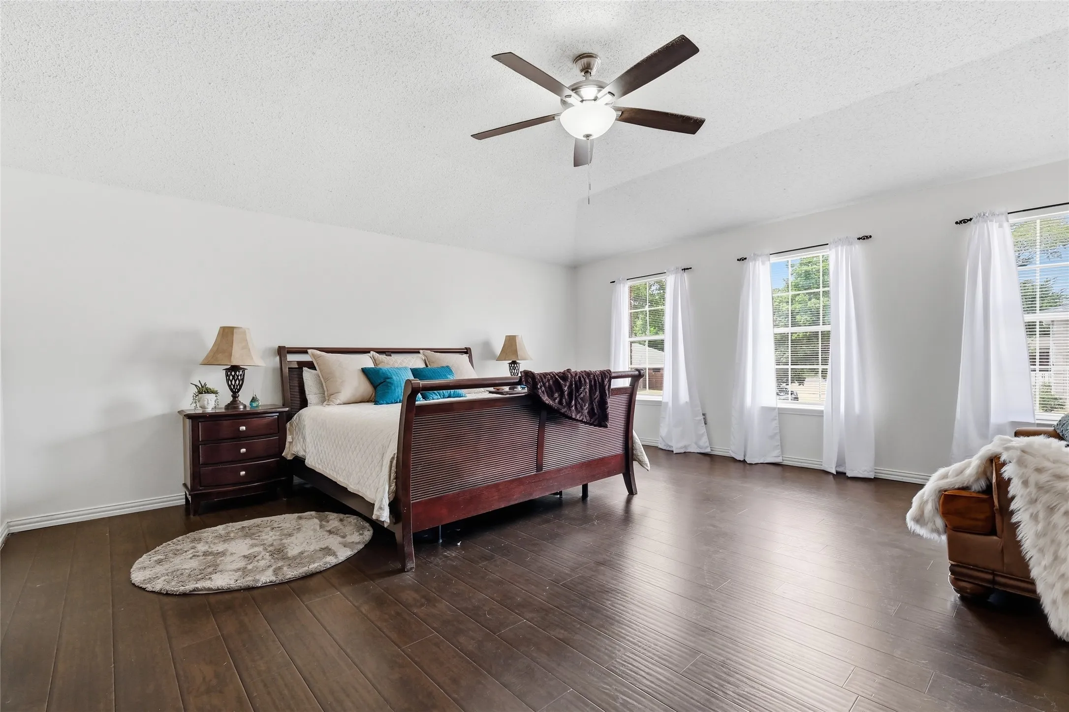 Spacious room featuring wood-finish flooring, multiple windows, a ceiling fan with integrated lighting, and white wall finishes