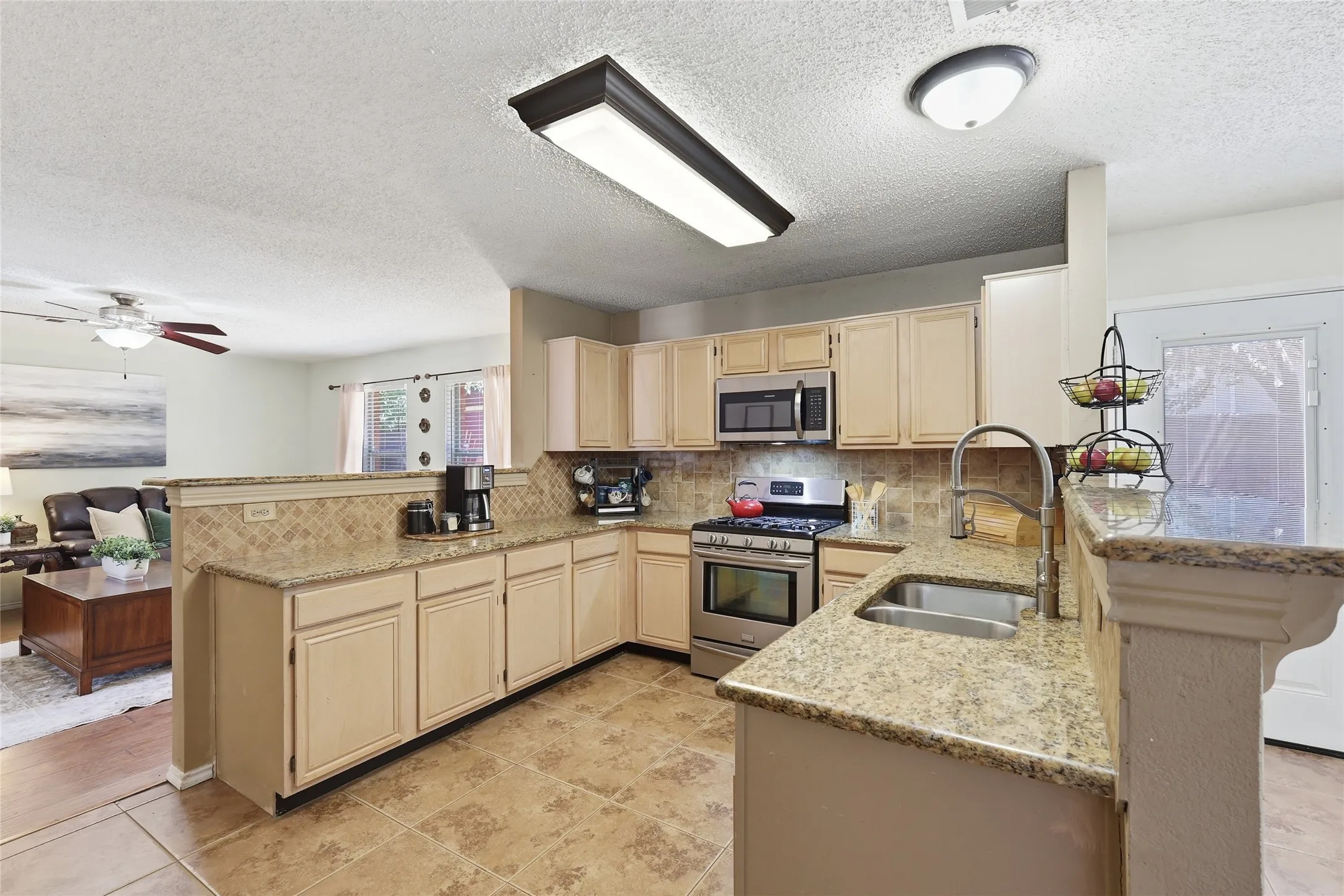 Kitchen featuring light-toned cabinetry, granite-finish countertops, stainless steel appliances, a tile backsplash, and tile flooring