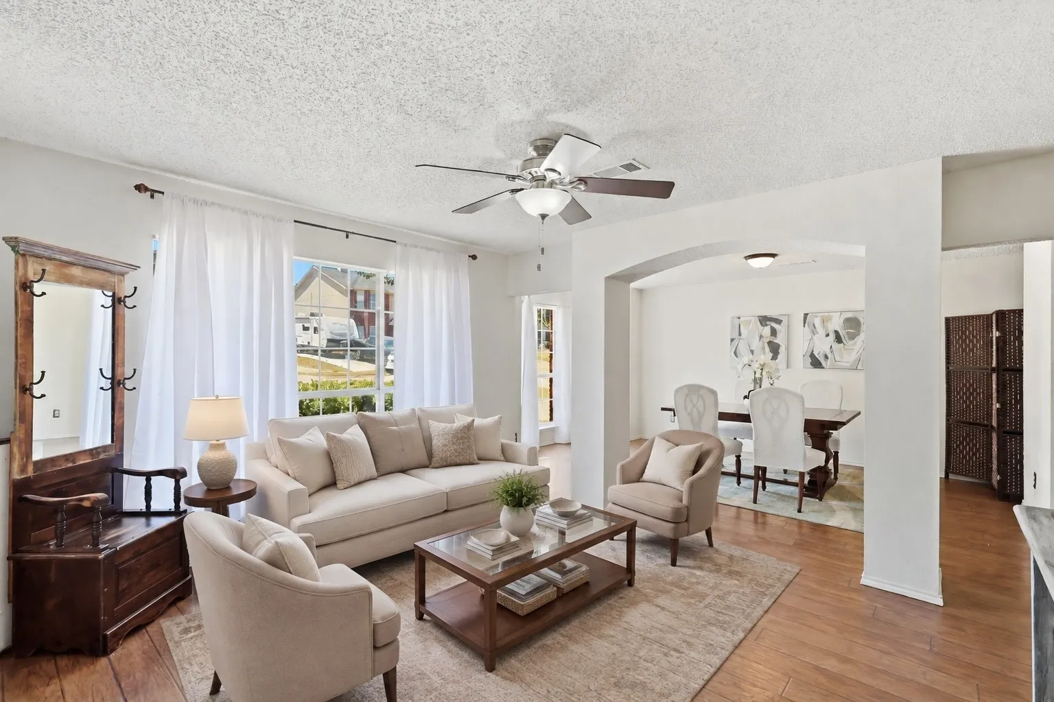 Light-filled living area featuring wood-finish flooring, a ceiling fan with integrated lighting, and an arched entryway