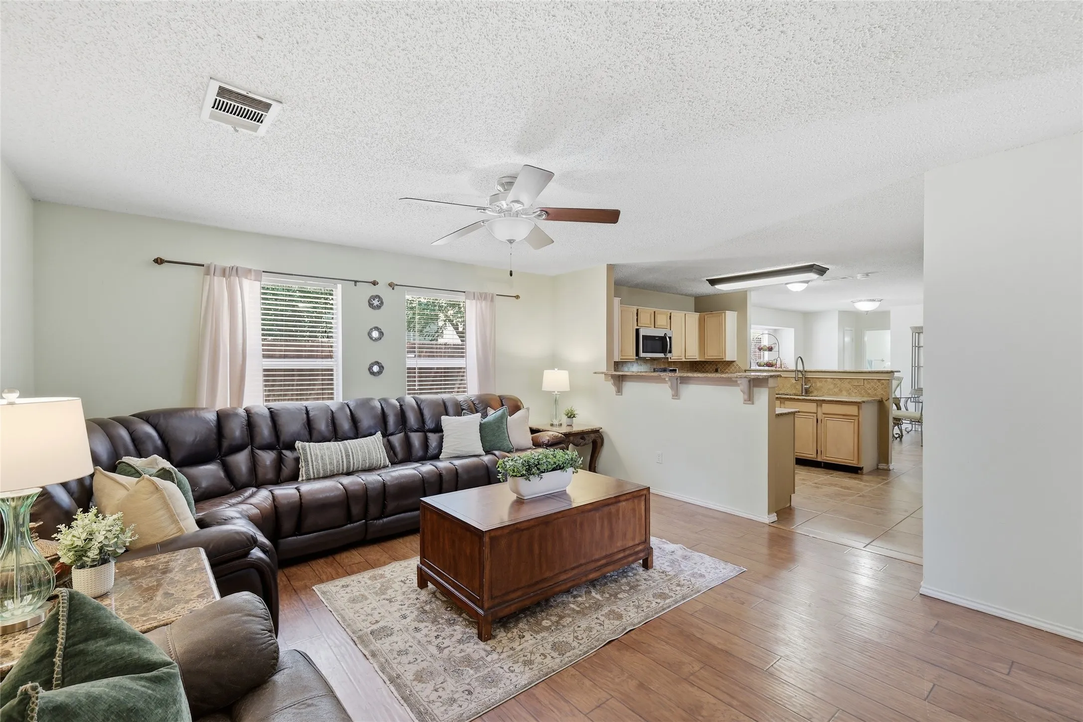 Wood-finish flooring throughout, ceiling fan, multiple windows with blinds, built-in kitchen cabinetry with microwave, and stone countertops