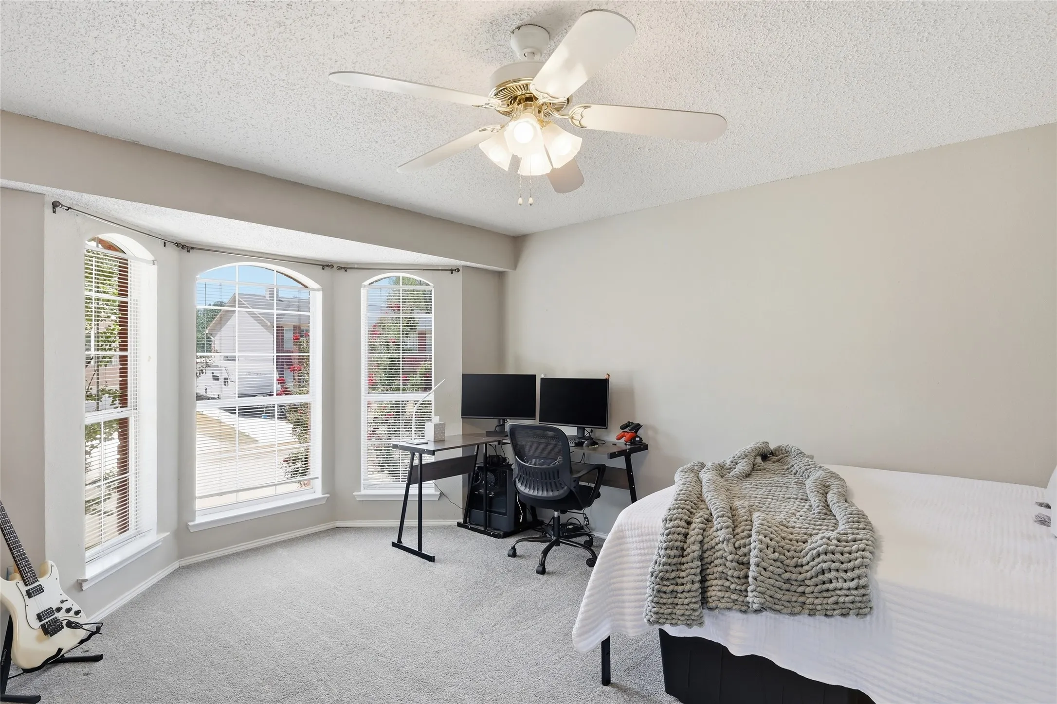Carpeted room featuring a ceiling fan with integrated lighting, a bay window with three arched upper panes, and light-toned walls