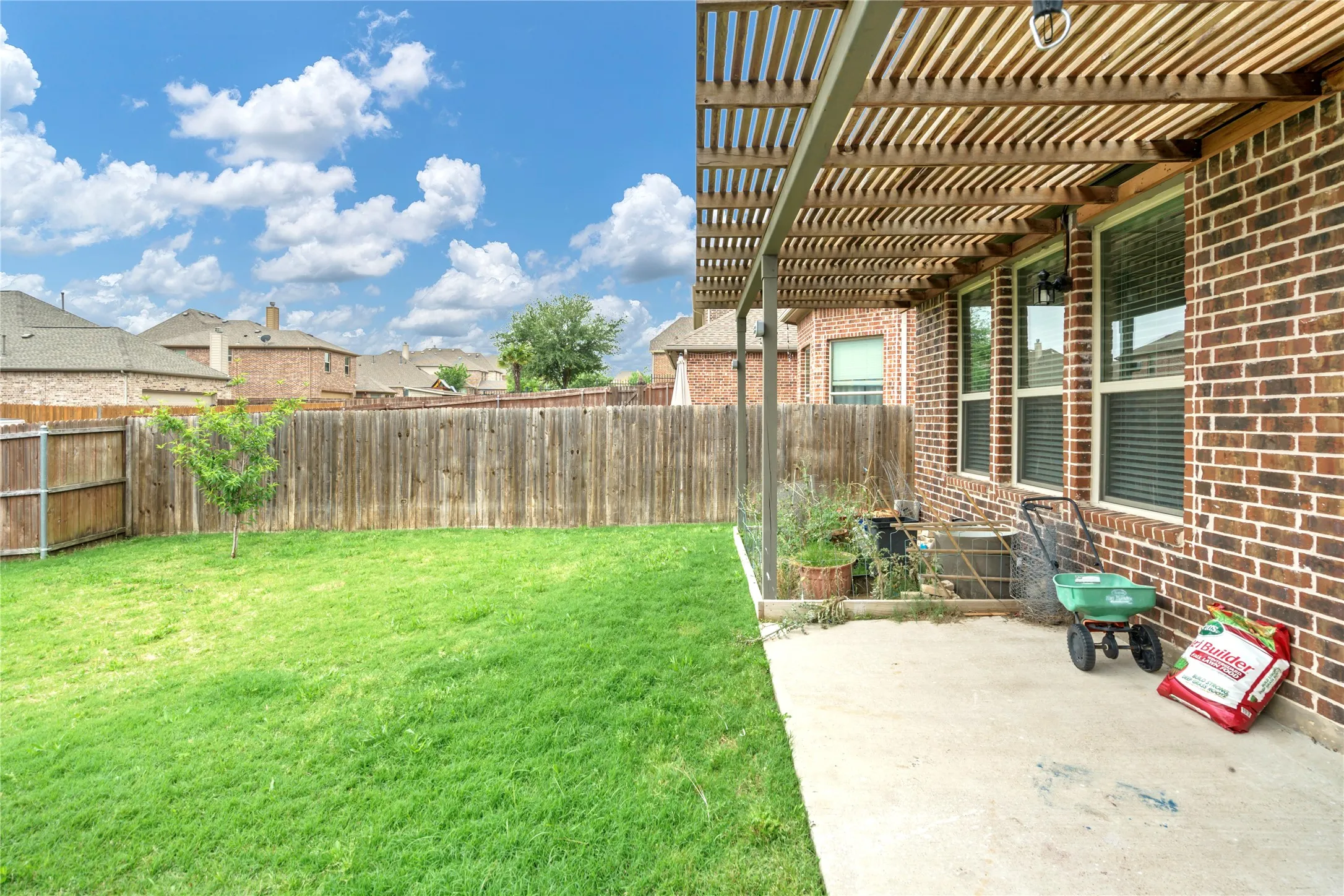 Expansive fenced yard featuring a concrete patio, wood pergola, and brick exterior