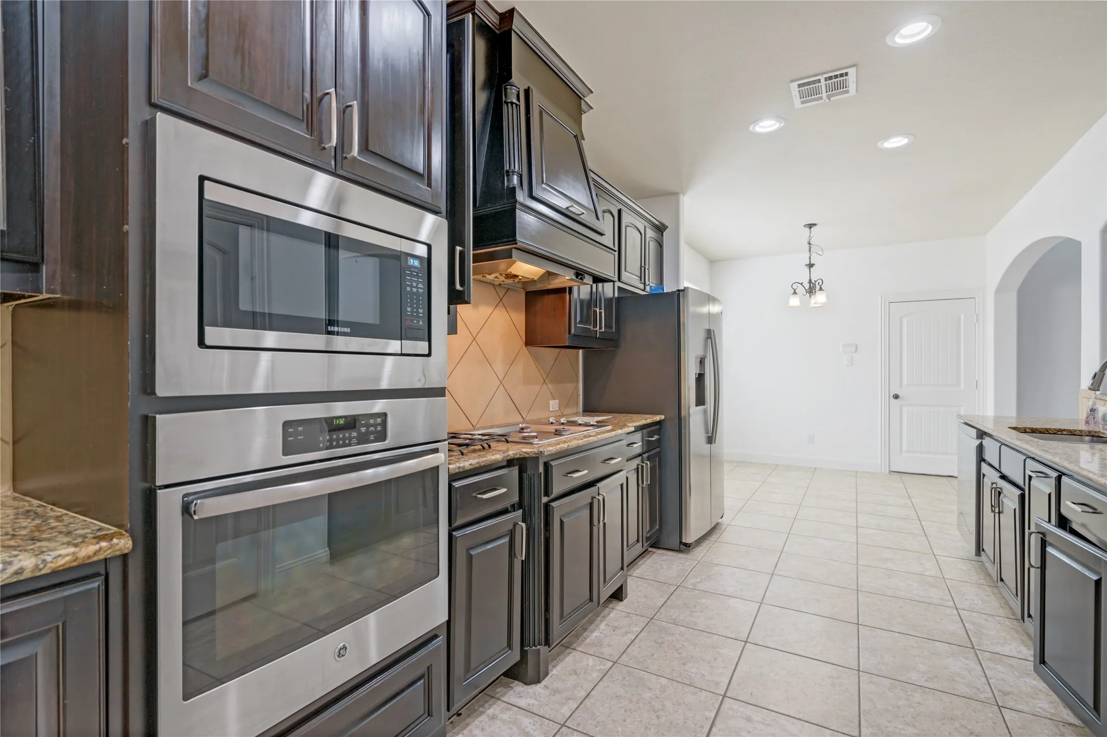 Stainless steel built-in microwave and oven, dark wood-finish cabinetry, granite countertops, and tile flooring