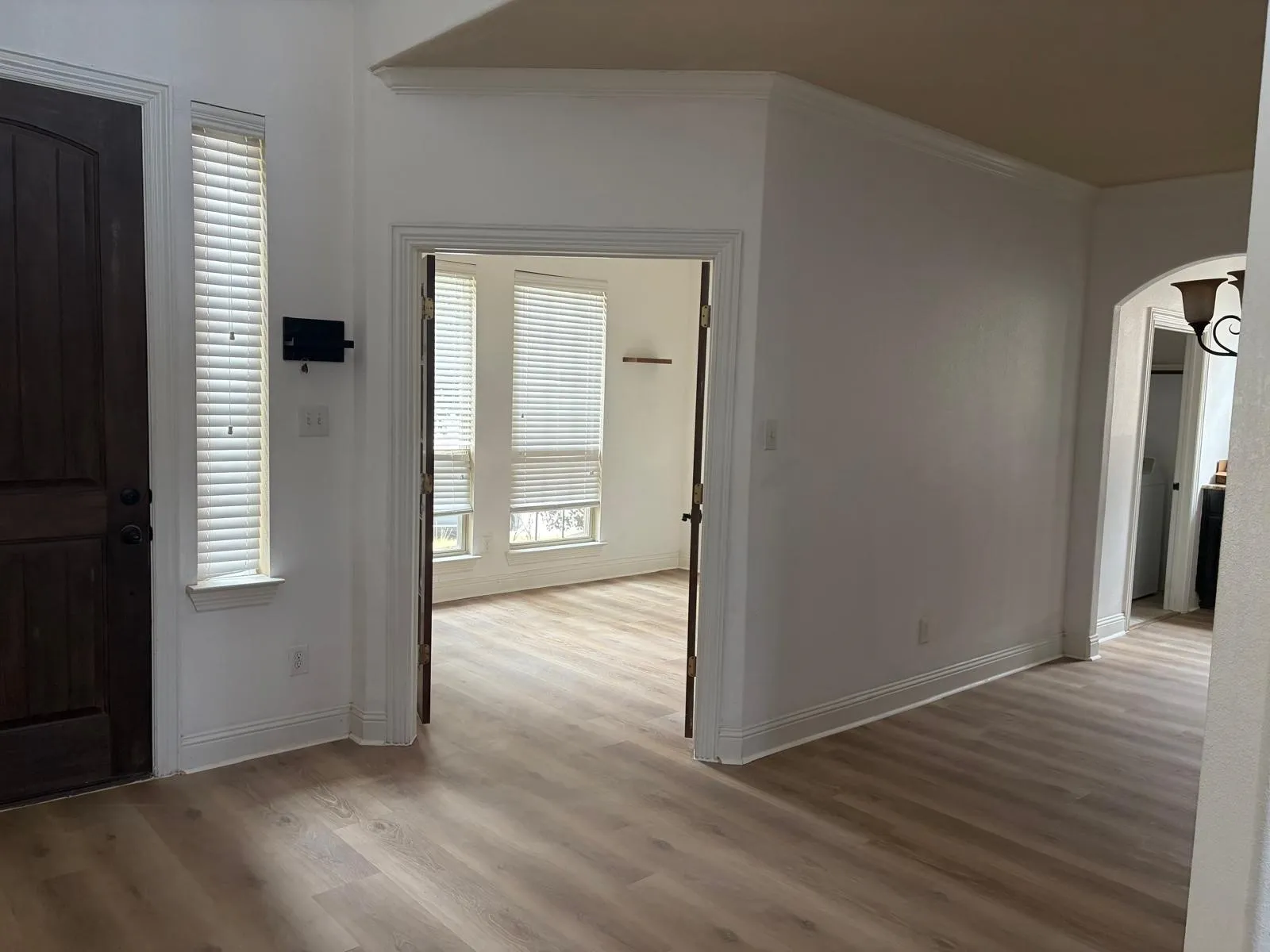 Wood-finish flooring throughout, arched entryway, crown molding, and bright windows with blinds