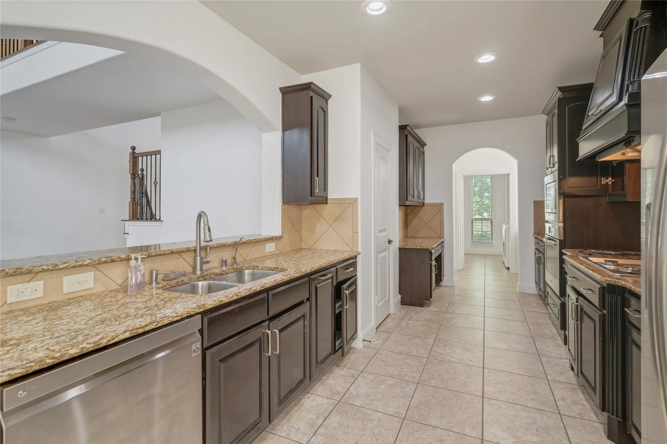 Kitchen featuring dark wood cabinetry, light granite countertops, stainless steel appliances, a tile backsplash, and recessed lighting