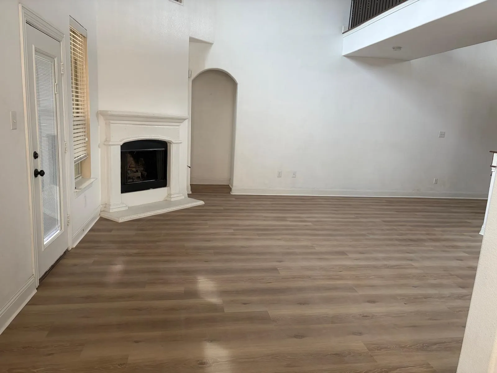 Vaulted ceiling, wood-finish flooring, white walls, arched doorway, and a fireplace with a white mantel and hearth