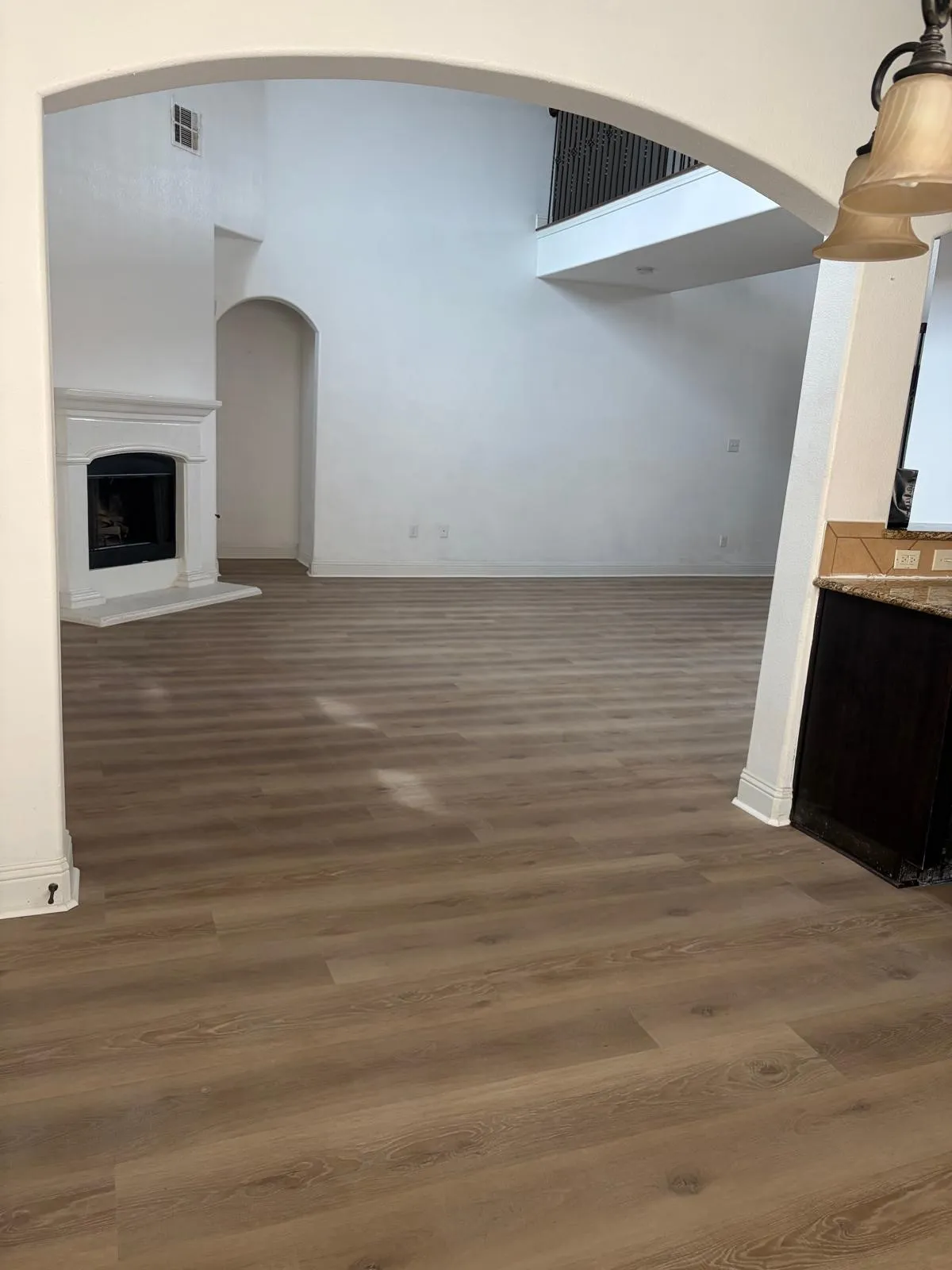 Expansive room featuring wood-finish flooring, a white mantel fireplace, and a high ceiling