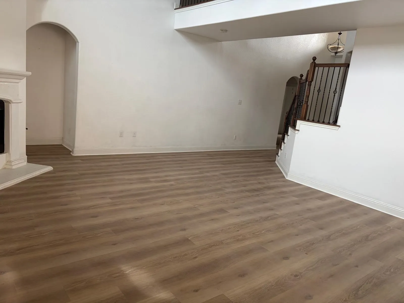Spacious room featuring wood-finish flooring, a white mantel, and an arched doorway