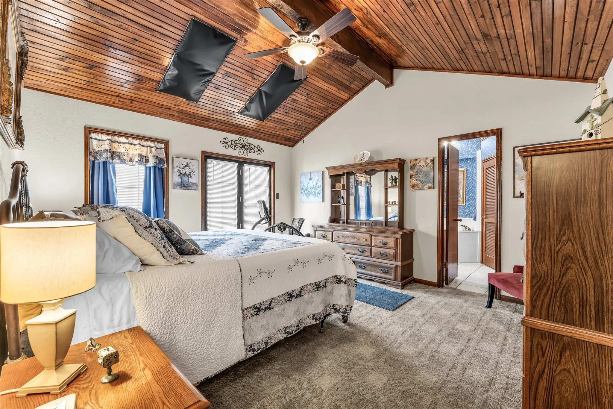 Vaulted wood-paneled ceiling with a ceiling fan, carpeted flooring, and a doorway opening to a tiled bathroom