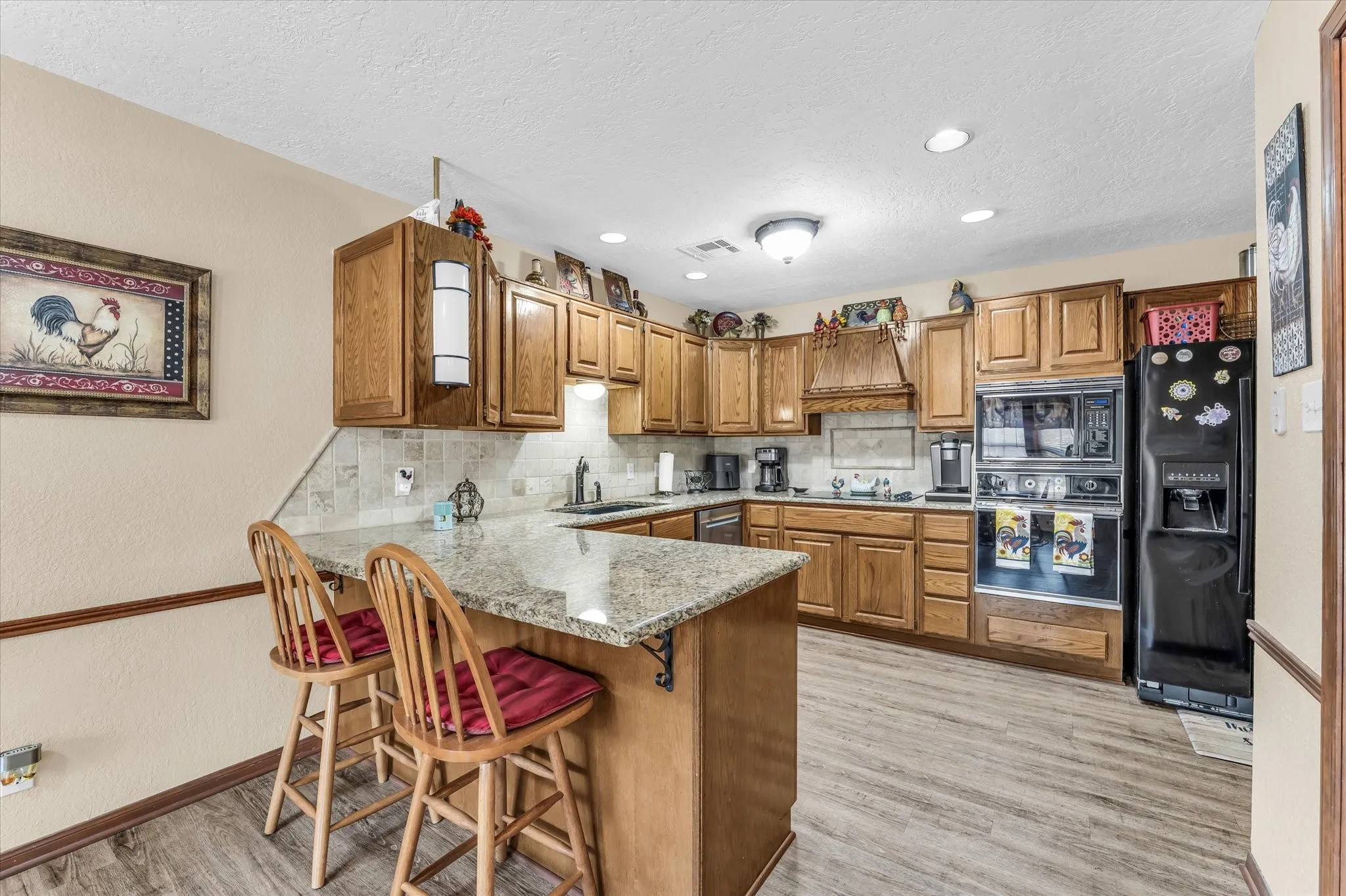 Kitchen featuring wood cabinetry, light-toned stone countertops, a tile backsplash, wood-finish flooring, and recessed lighting