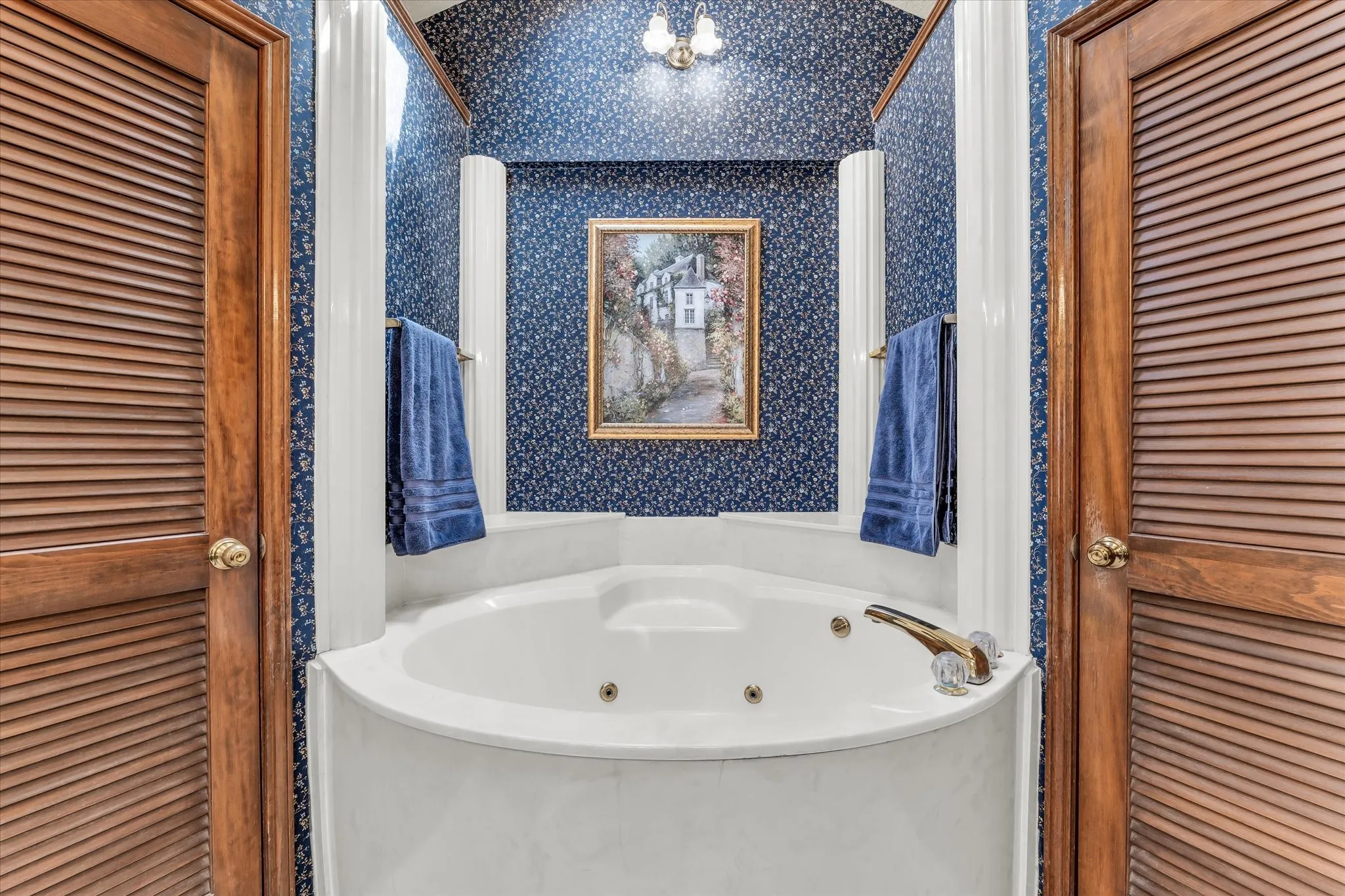 Corner jetted tub featuring a deck-mounted faucet and a tiled surround