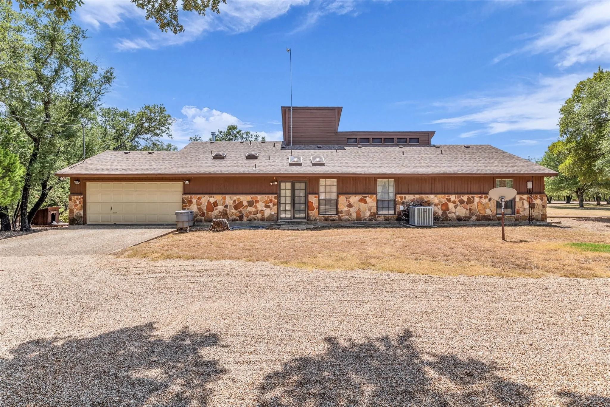 Exterior featuring stone and horizontal siding, a two-car garage, and a gravel driveway