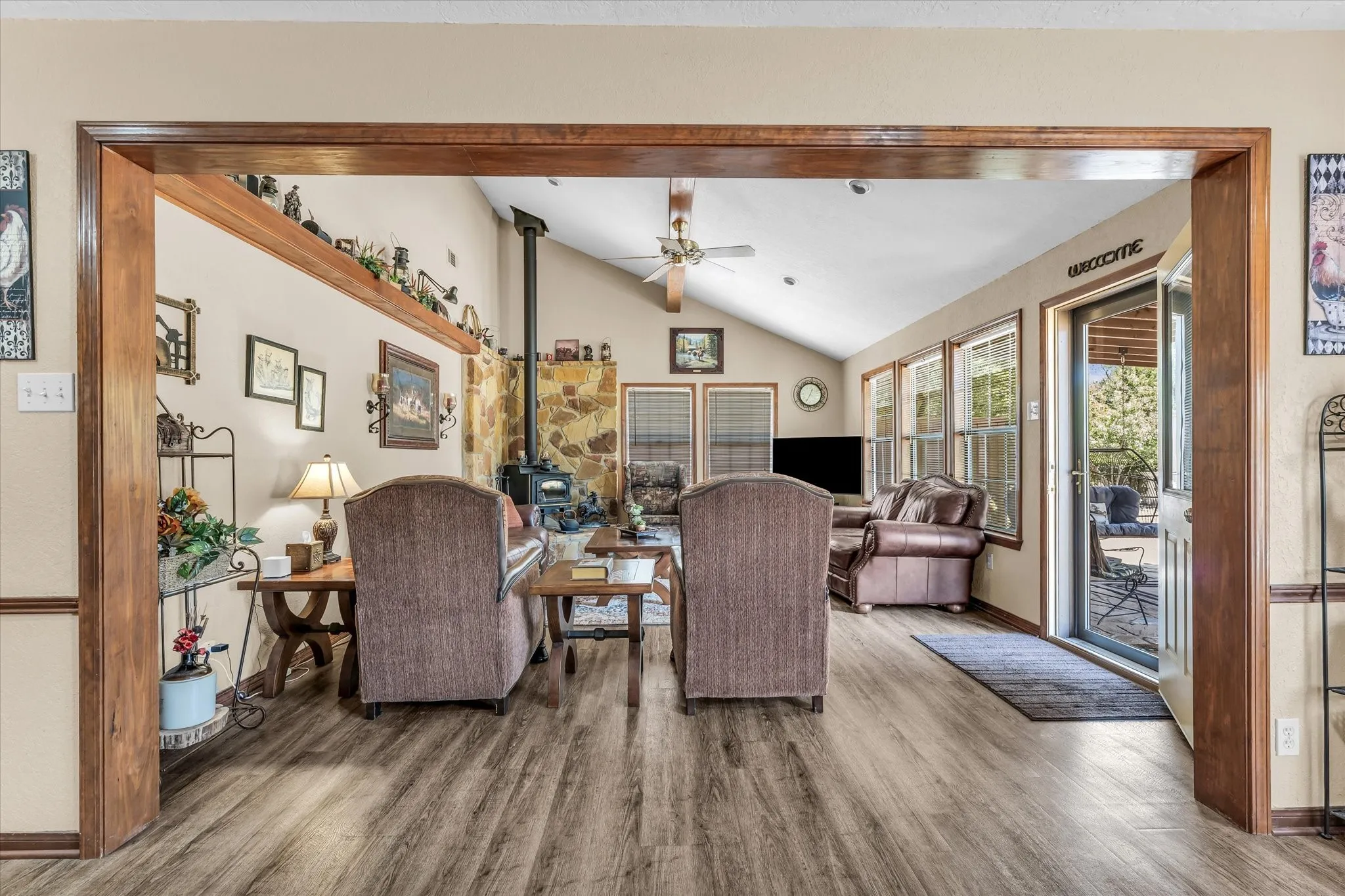 Spacious living area featuring wood-finish flooring, a vaulted ceiling, multiple windows, and a glass-paned exterior door