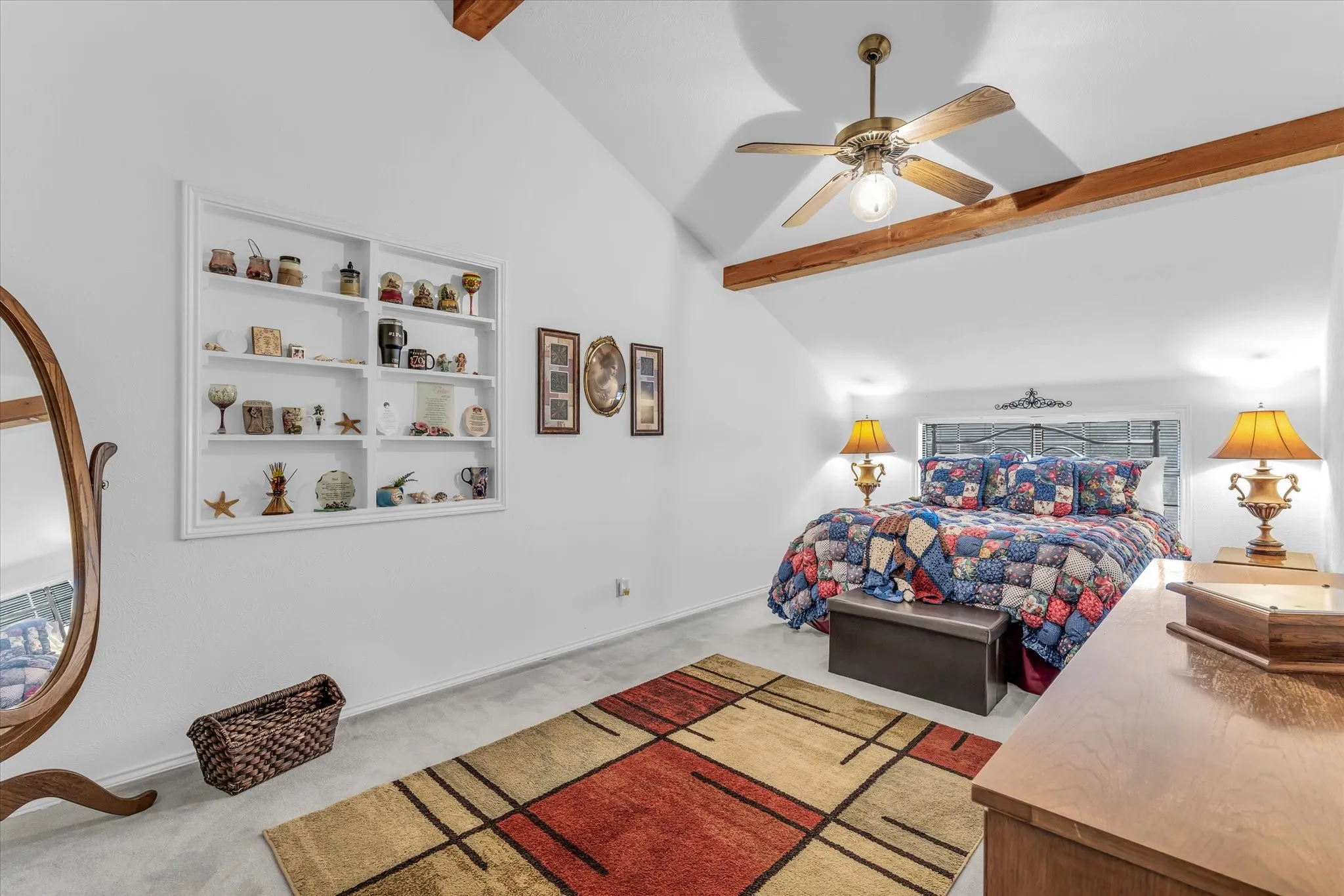 Vaulted ceiling with exposed wood beams, ceiling fan, built-in shelving, and carpeted flooring