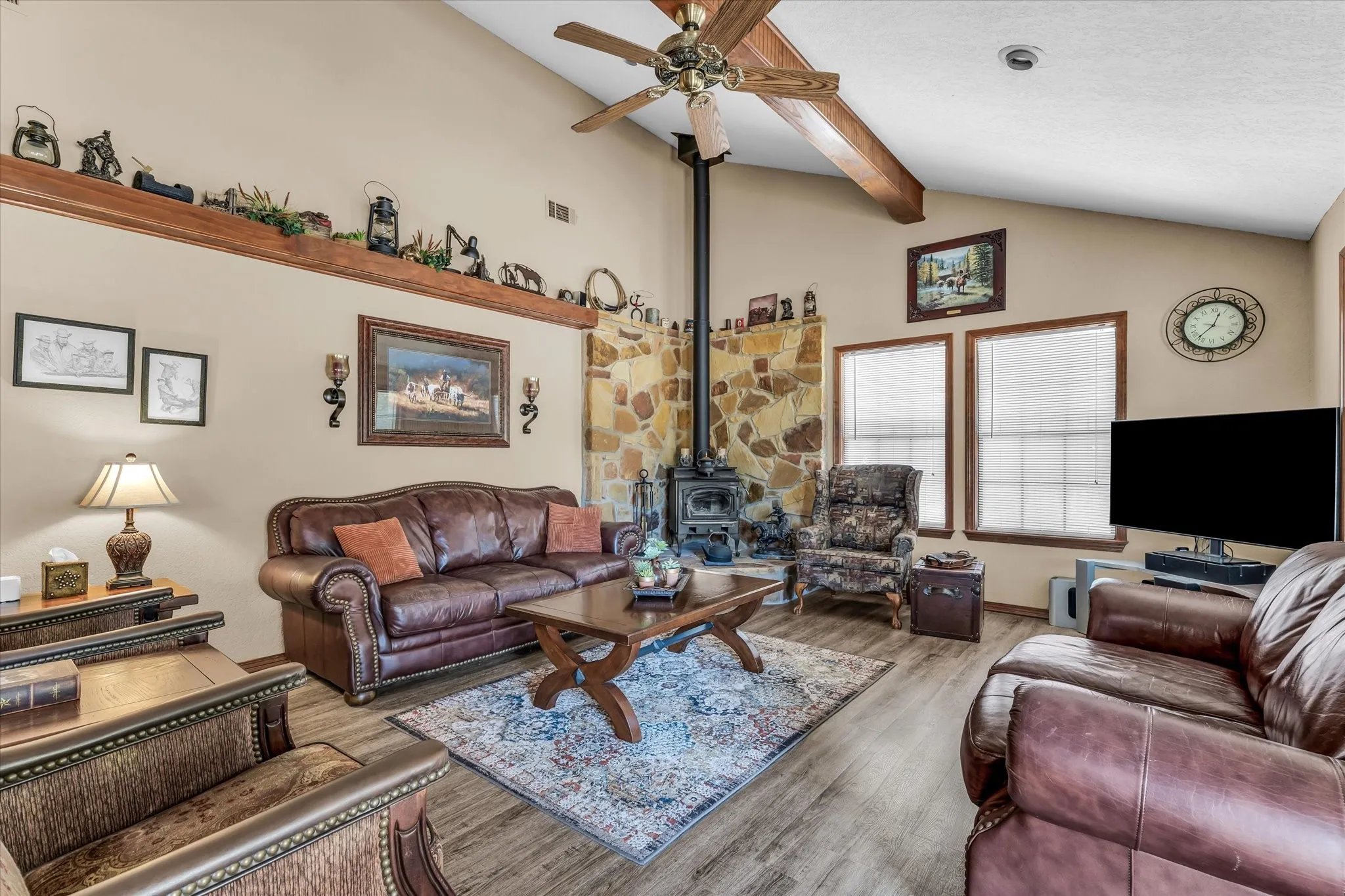 Vaulted ceiling with a wood-finish beam, stone-clad fireplace, wood-finish flooring, and multiple windows
