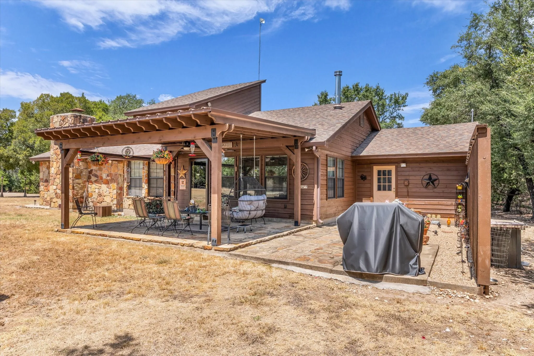 Stone and wood-sided exterior featuring a stone chimney, covered patio with wood pergola, and an additional open patio space