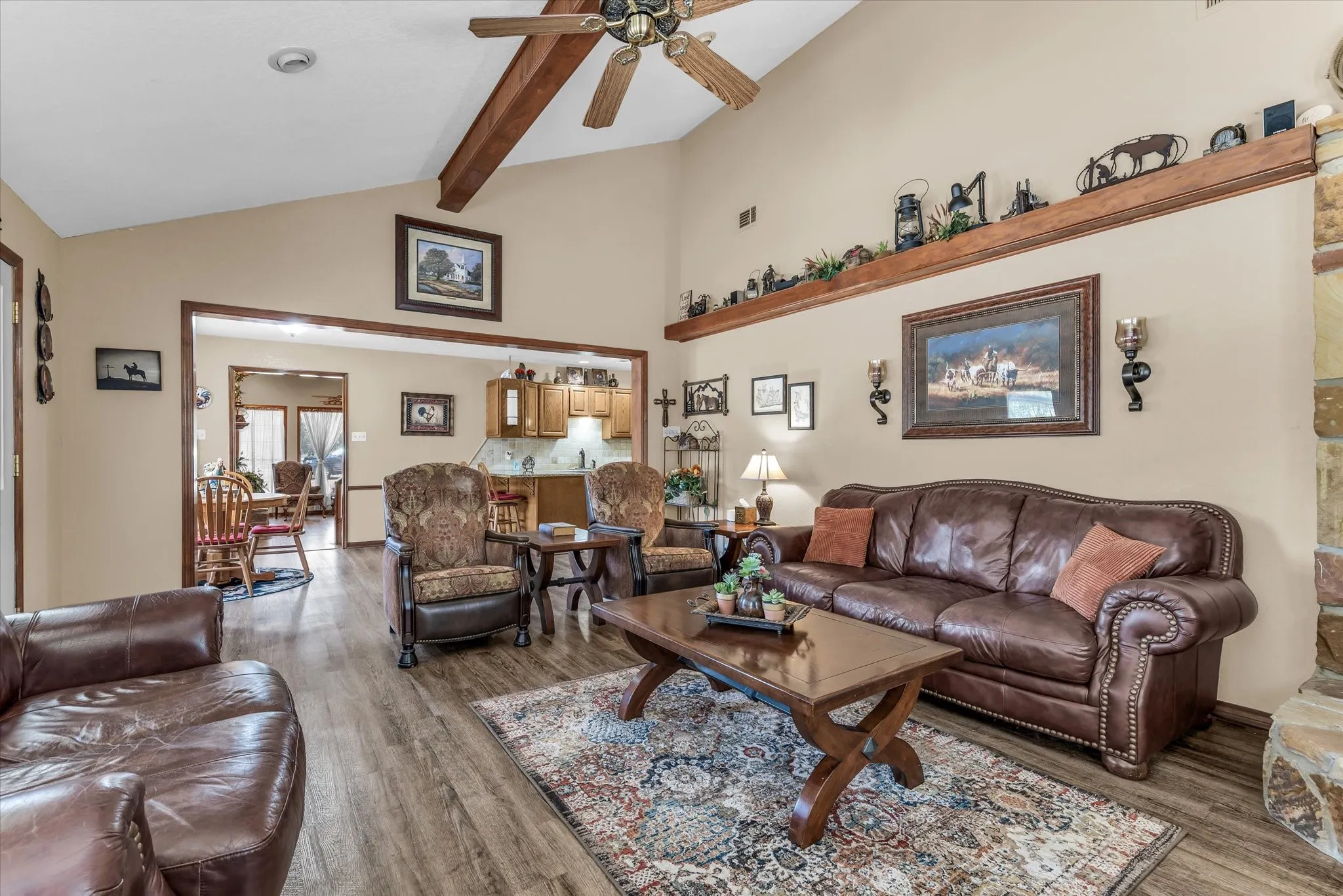 Vaulted ceiling with exposed wood beams, wood-finish flooring, recessed lighting, and a stone-clad fireplace surround