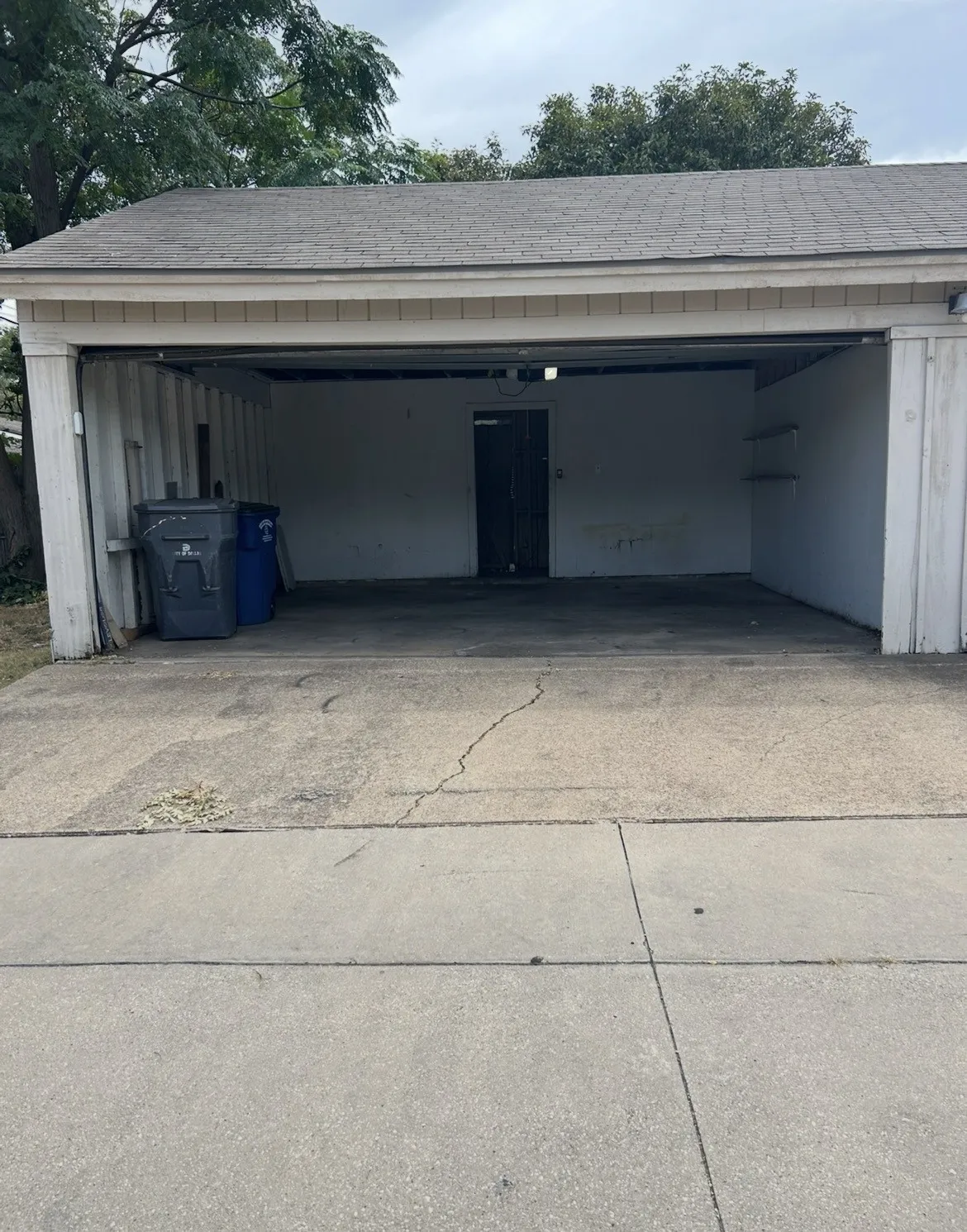 Attached two-car garage with a concrete floor, built-in shelving, and a shingle roof