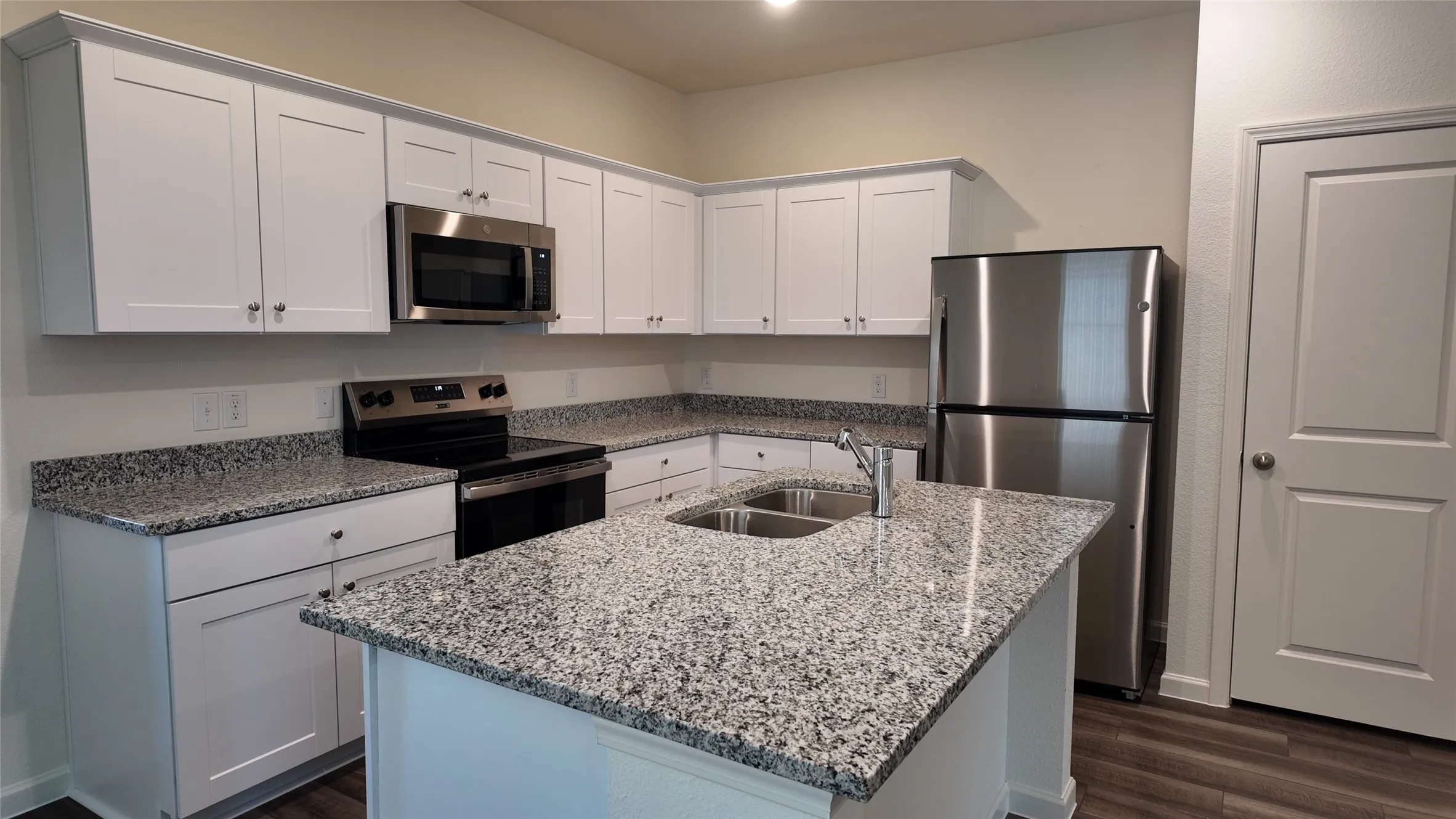 Kitchen featuring white shaker-style cabinetry, granite countertops, stainless steel appliances, and a central island with an integrated sink