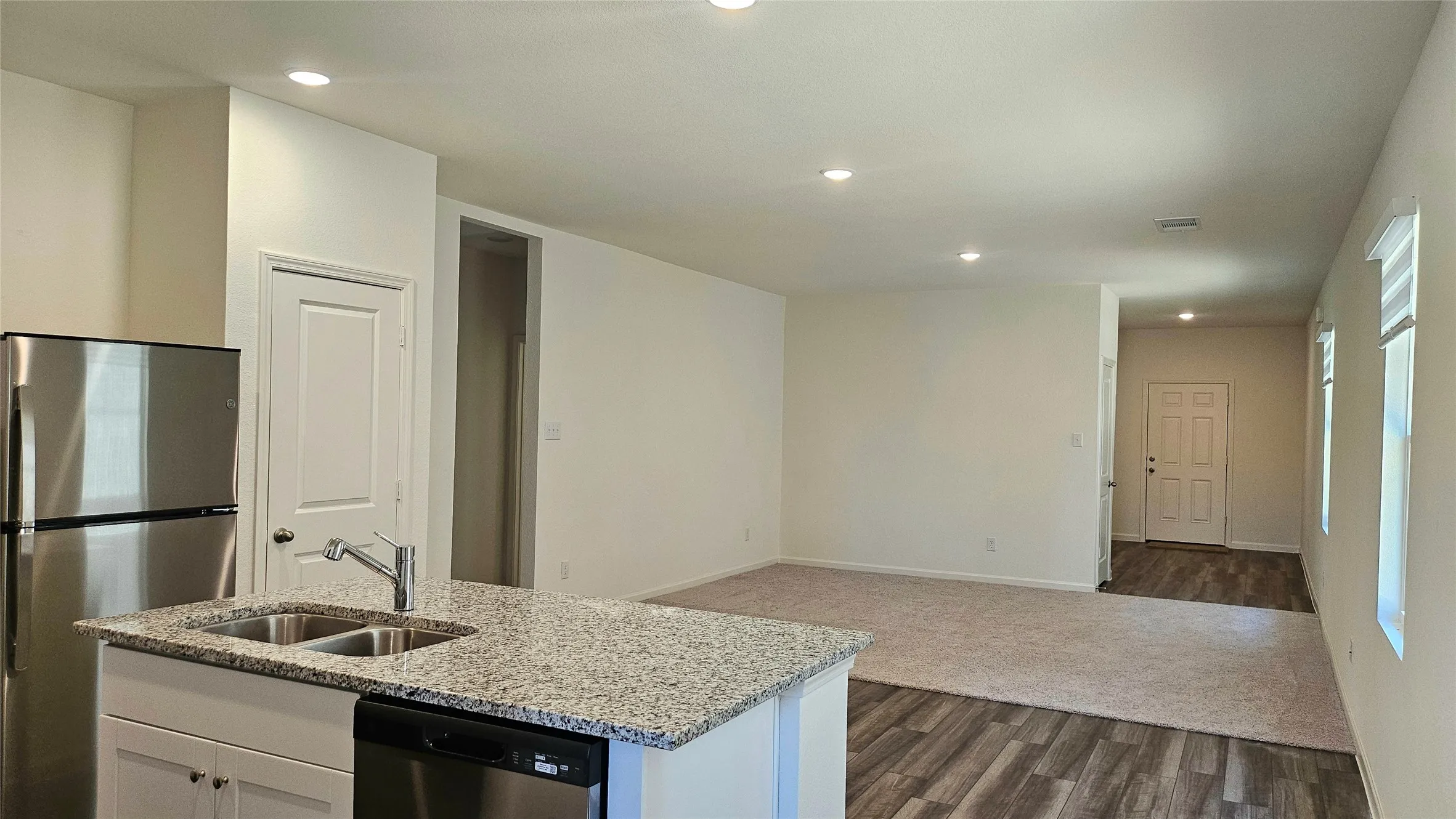 Kitchen island featuring a dual basin stainless steel sink and granite-finish countertop, stainless steel refrigerator, and recessed lighting