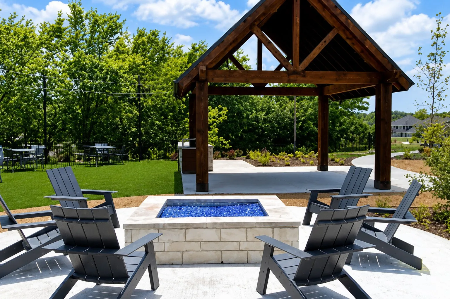 Outdoor fire pit featuring a stone base and blue glass media, complemented by a timber-framed pavilion