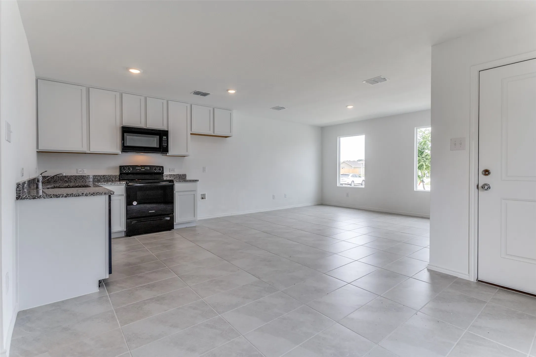 Kitchen with white cabinets, sink, light tile floors, and black appliances