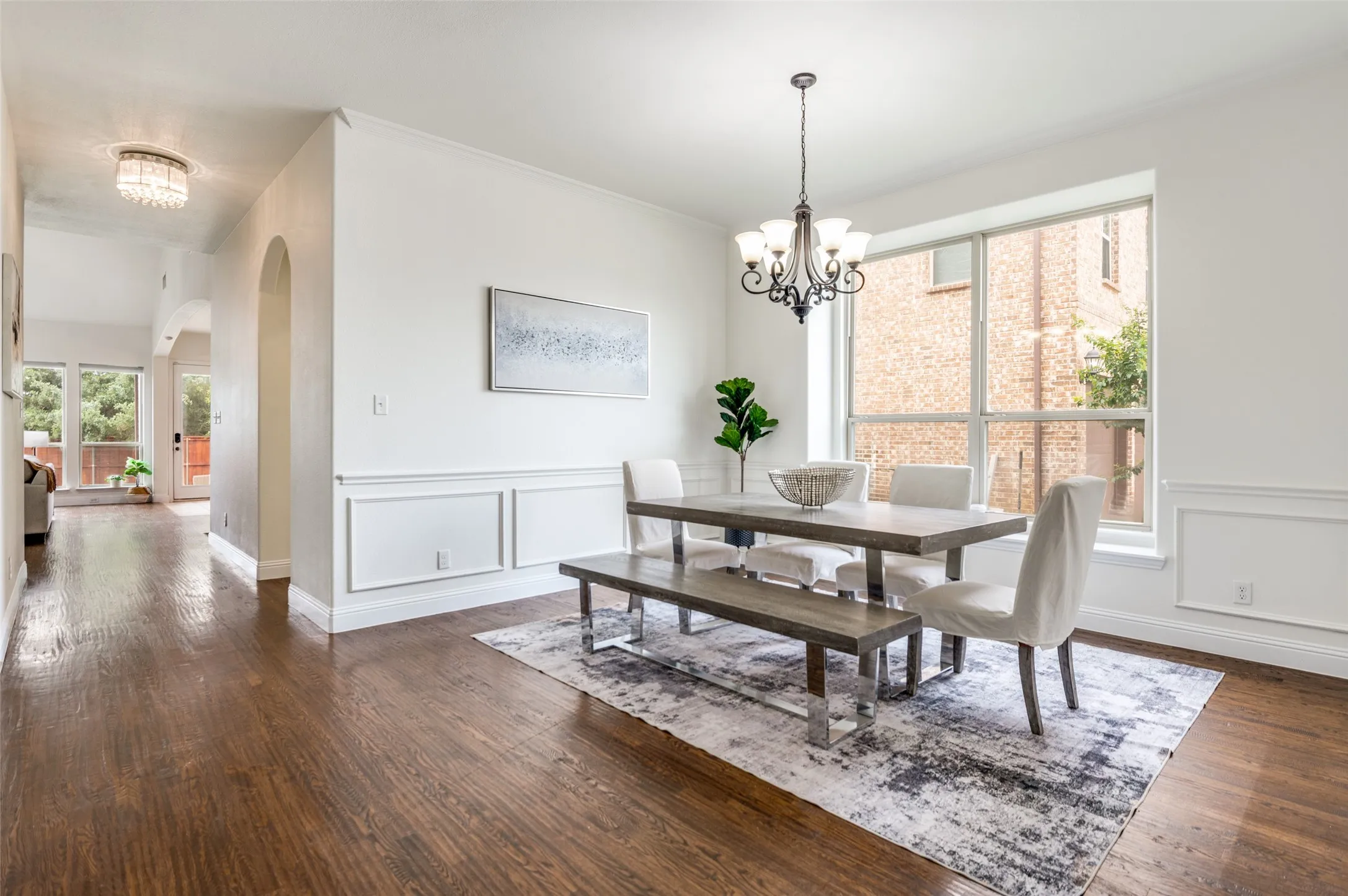 Hardwood-finish flooring, decorative wall molding, arched entryway, contemporary chandelier, and large window