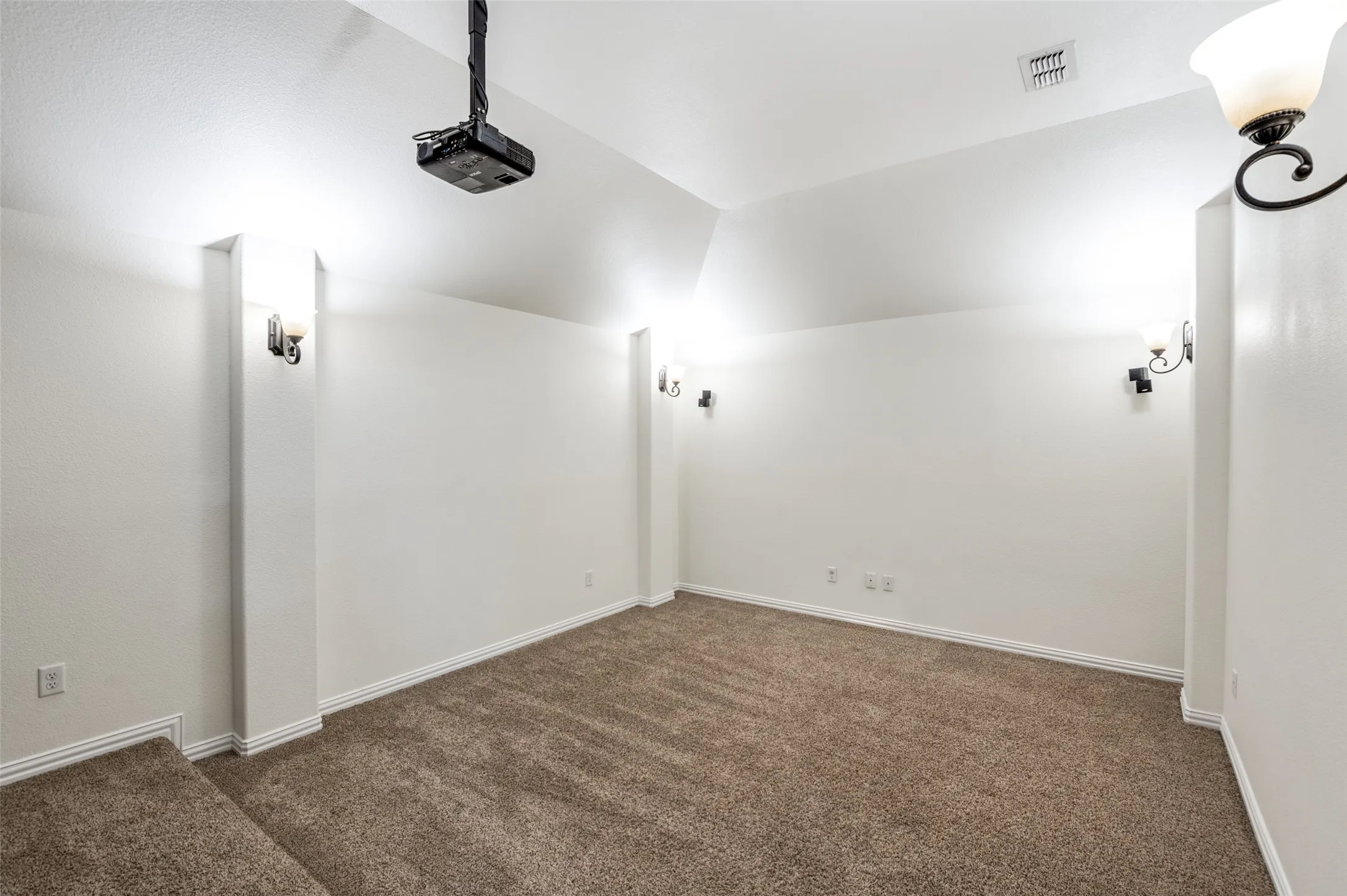 Recessed projector, wall-mounted sconce lighting, vaulted ceiling, and carpeted flooring