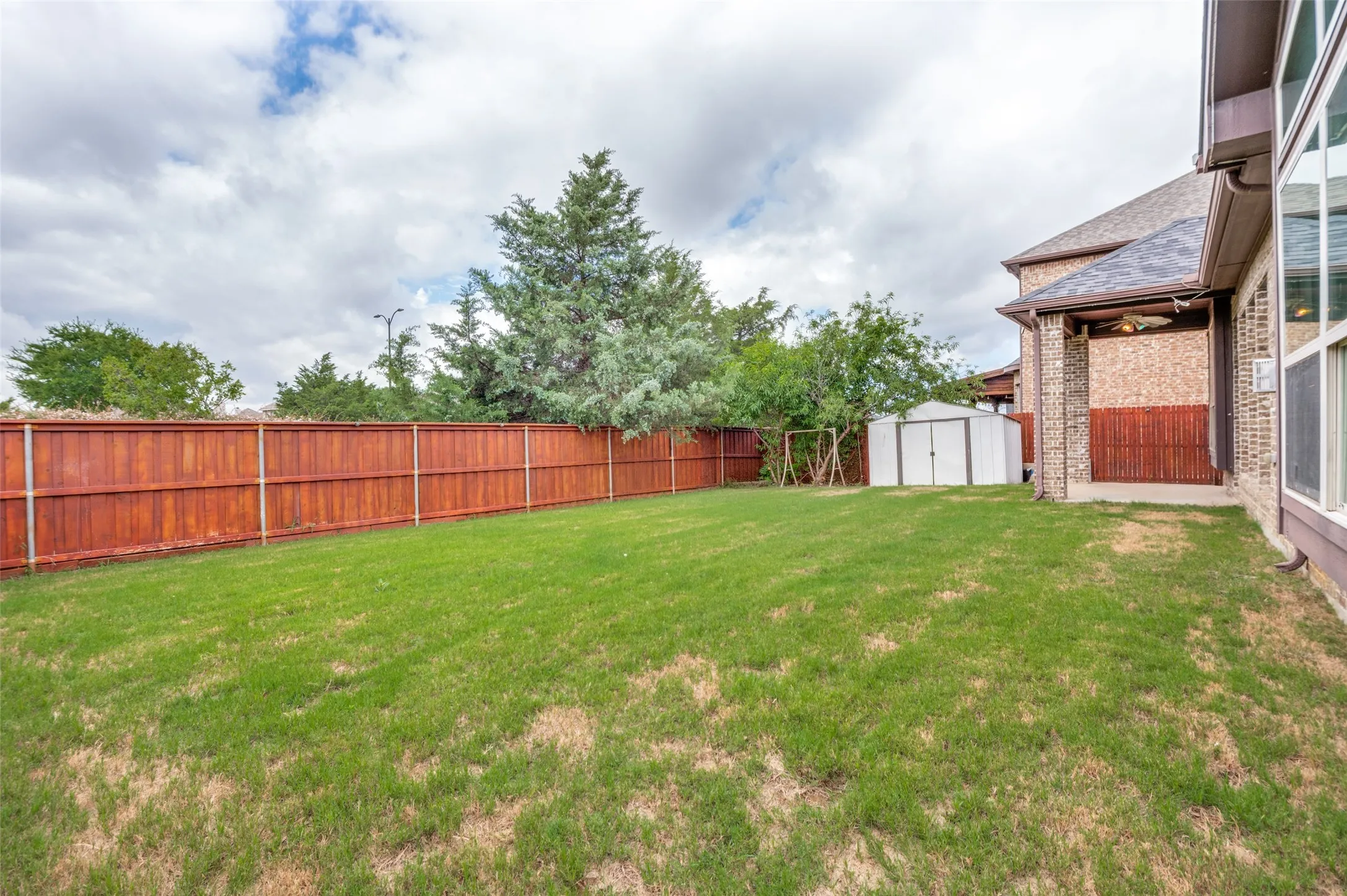 Expansive backyard featuring a manicured lawn, a privacy fence, and a storage shed