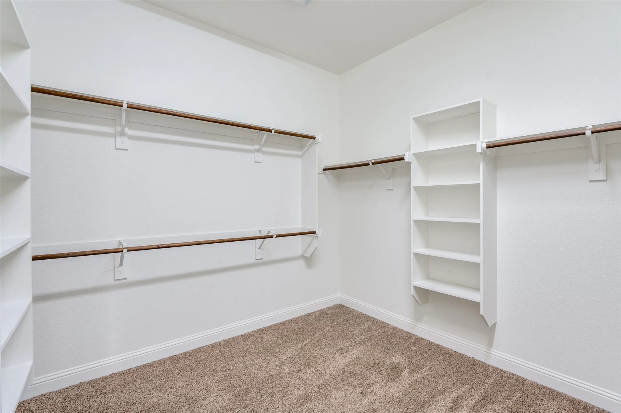 Spacious closet with built-in shelving, multiple hanging rods, and neutral-toned carpeting