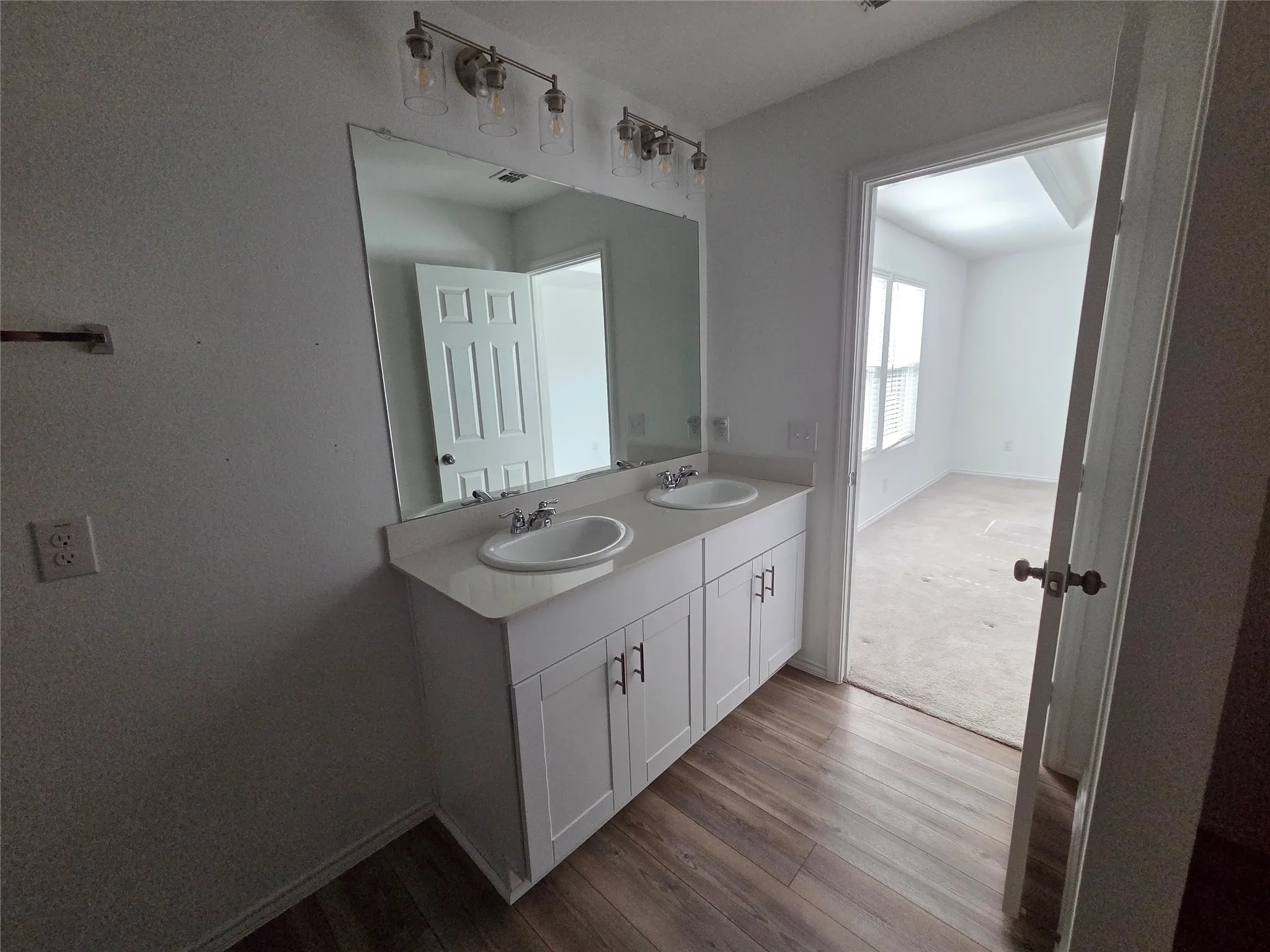 Double vanity with undermount sinks, white cabinetry, a large wall-mounted mirror, and wood-finish flooring