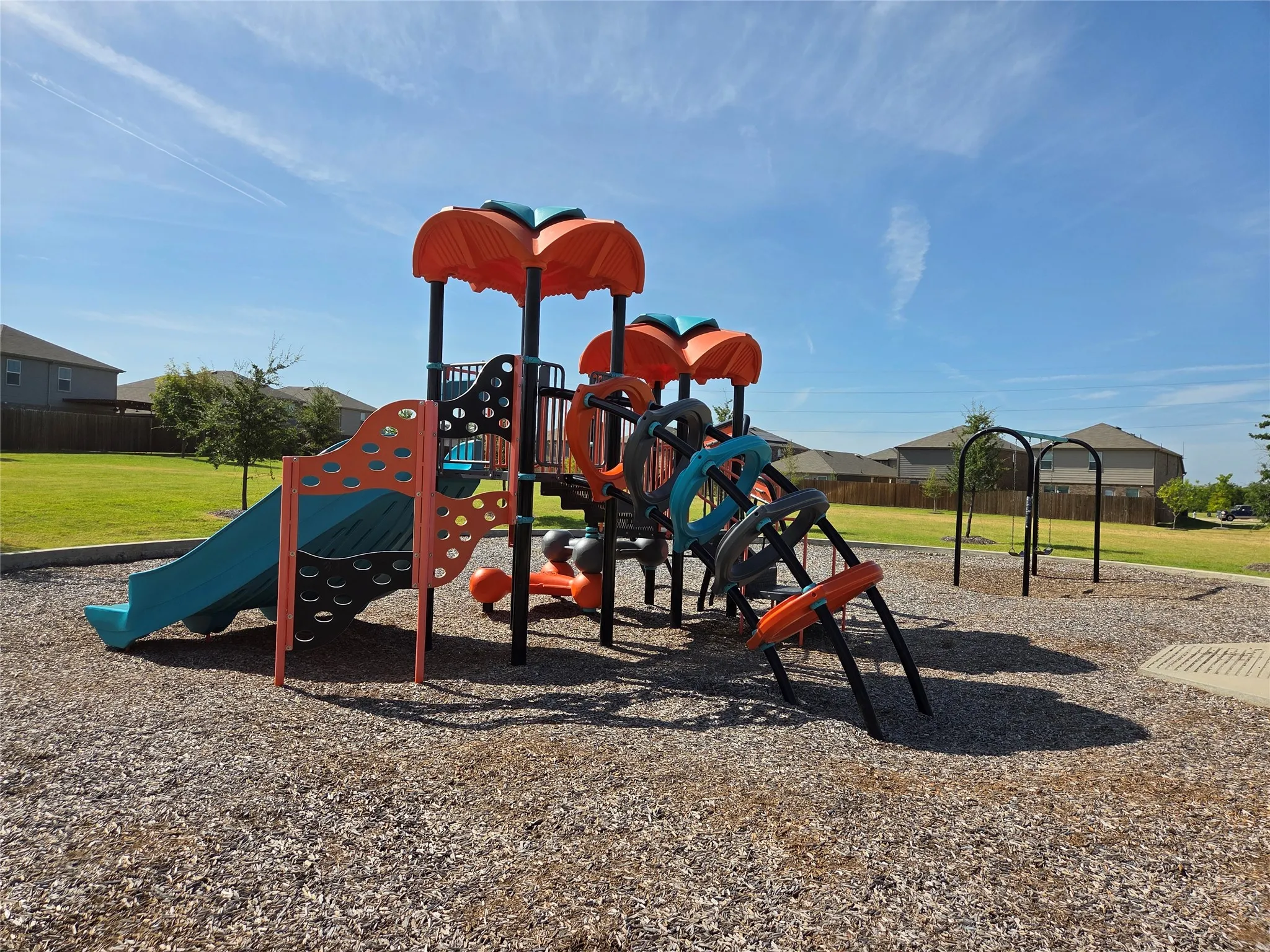 Community playground with multi-color play structures, a slide, and swing set