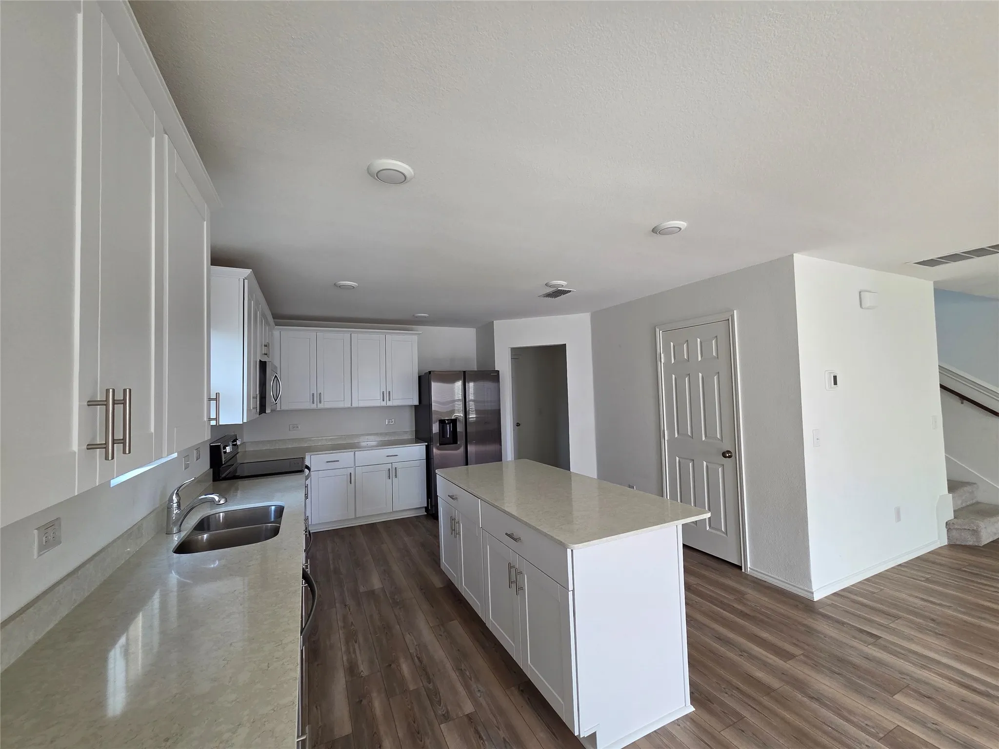 Contemporary kitchen featuring white cabinetry, light-toned countertops, stainless steel appliances, a center island, and wood-finish flooring