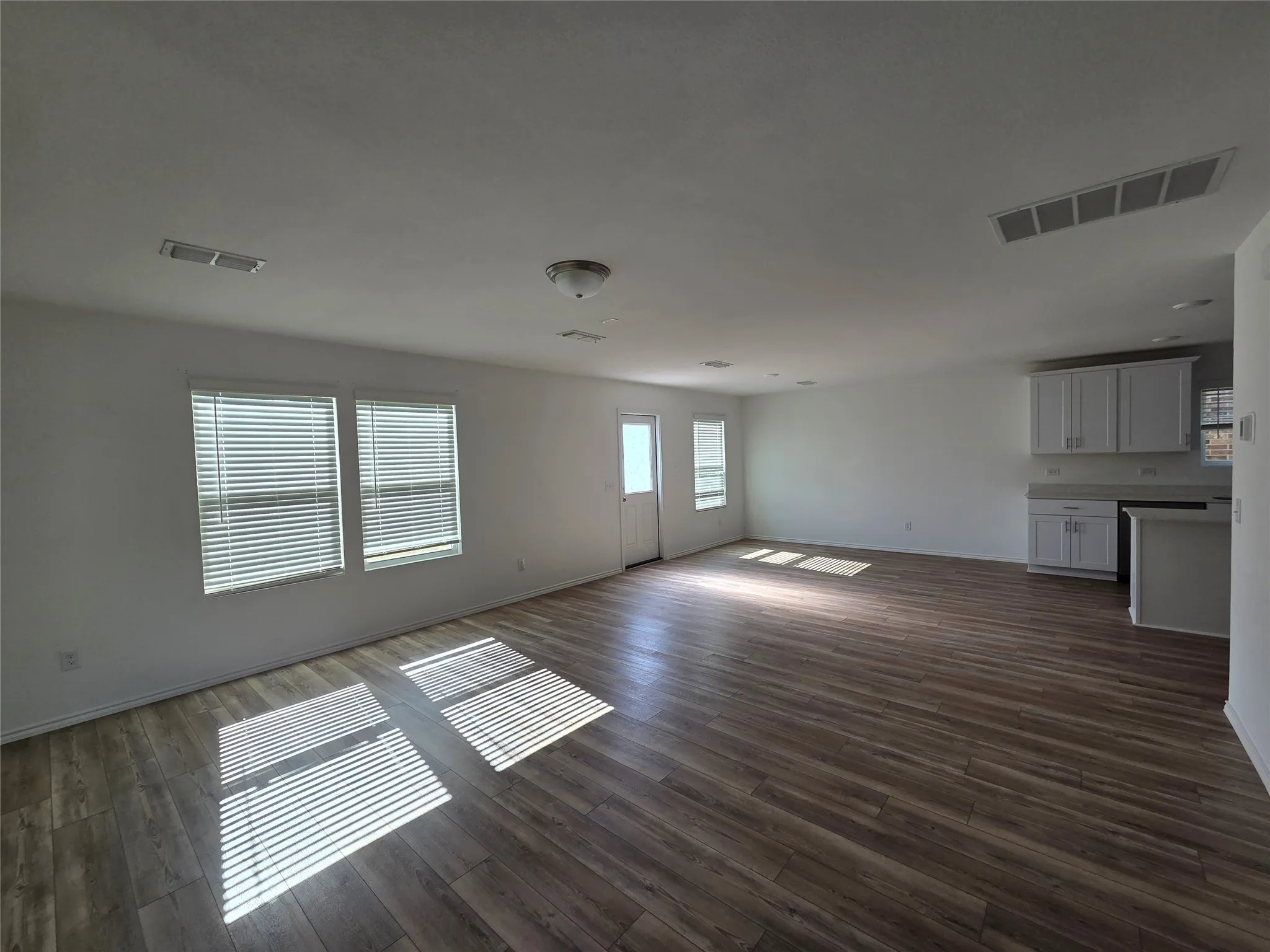 Open-concept living space featuring wood-finish flooring, white walls, multiple windows with blinds, and white cabinetry