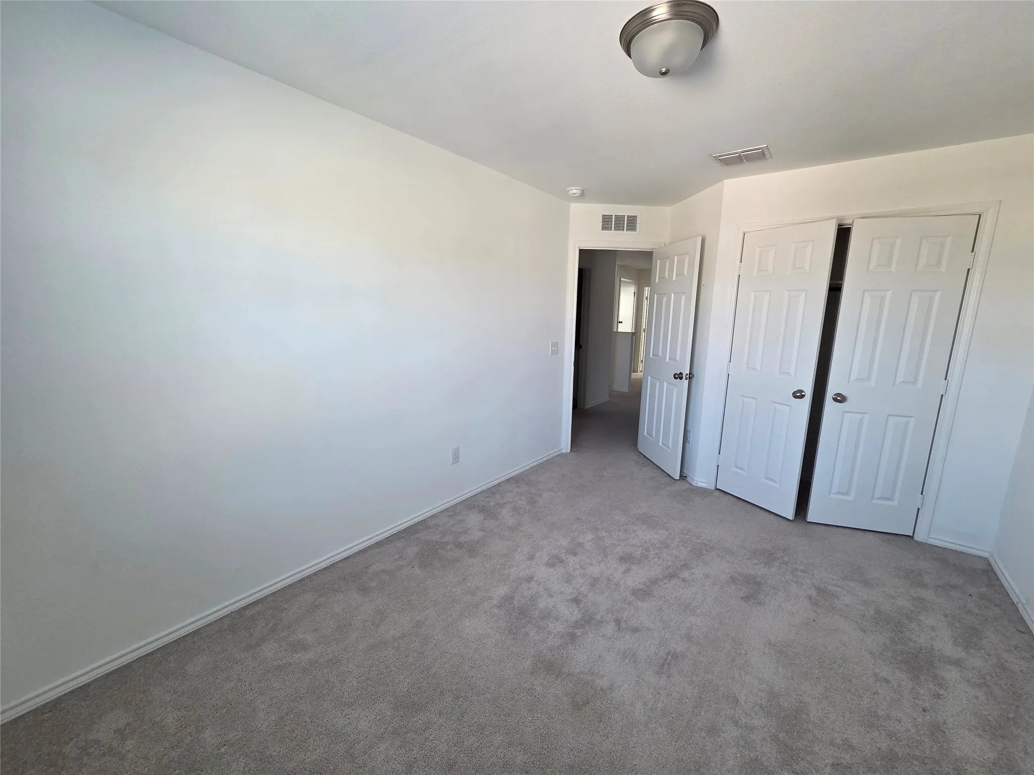 Neutral-toned carpeting, white walls, white paneled doors, and a flush mount ceiling light fixture
