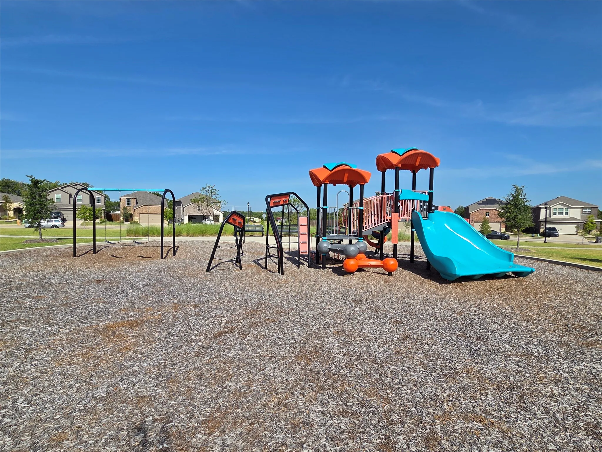 Community playground featuring multiple swings, a vibrant slide, and climbing structures on a wood chip surface