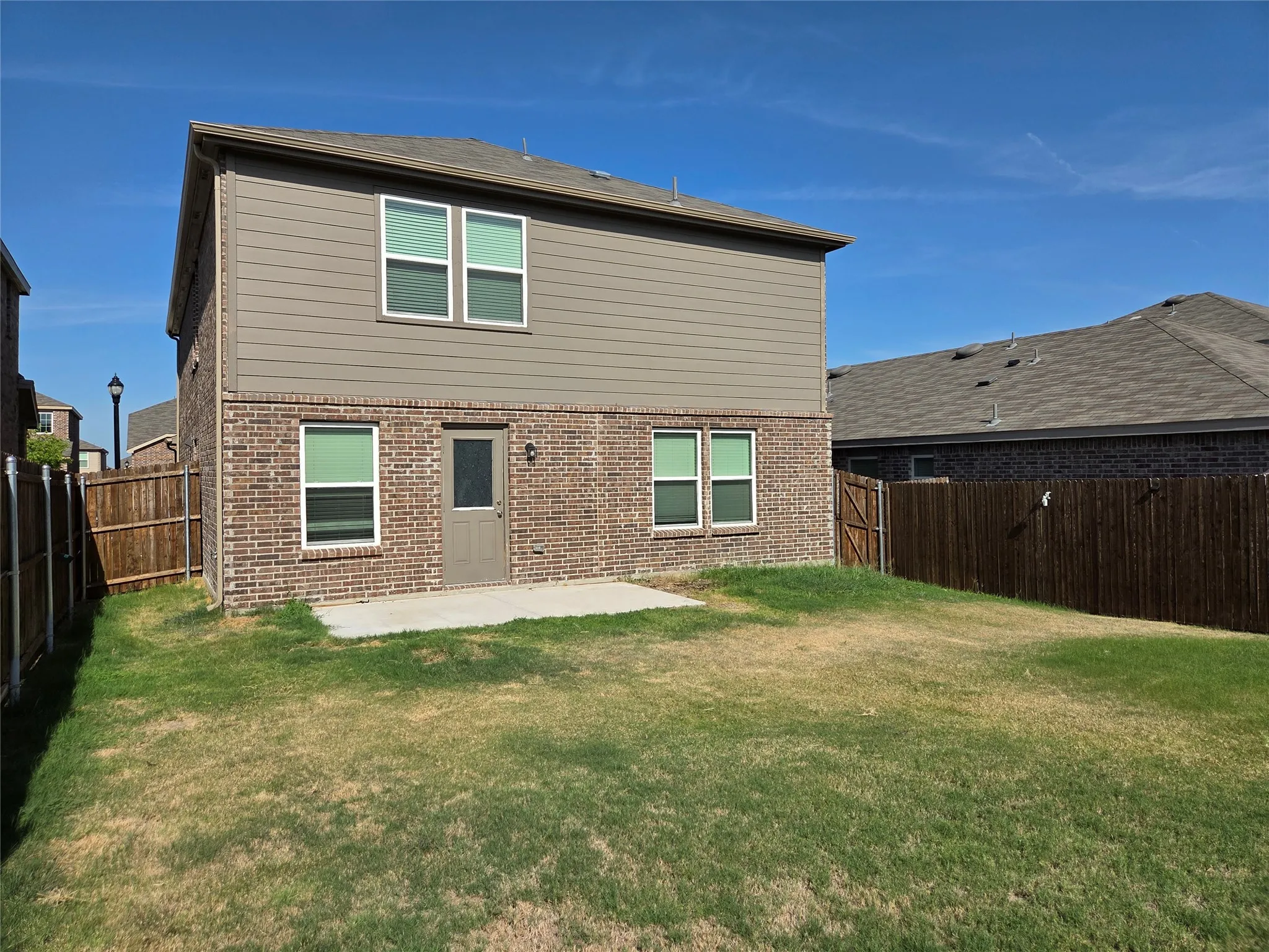 Rear exterior with a brick and siding facade, multiple windows, a rear entry door, and a concrete patio