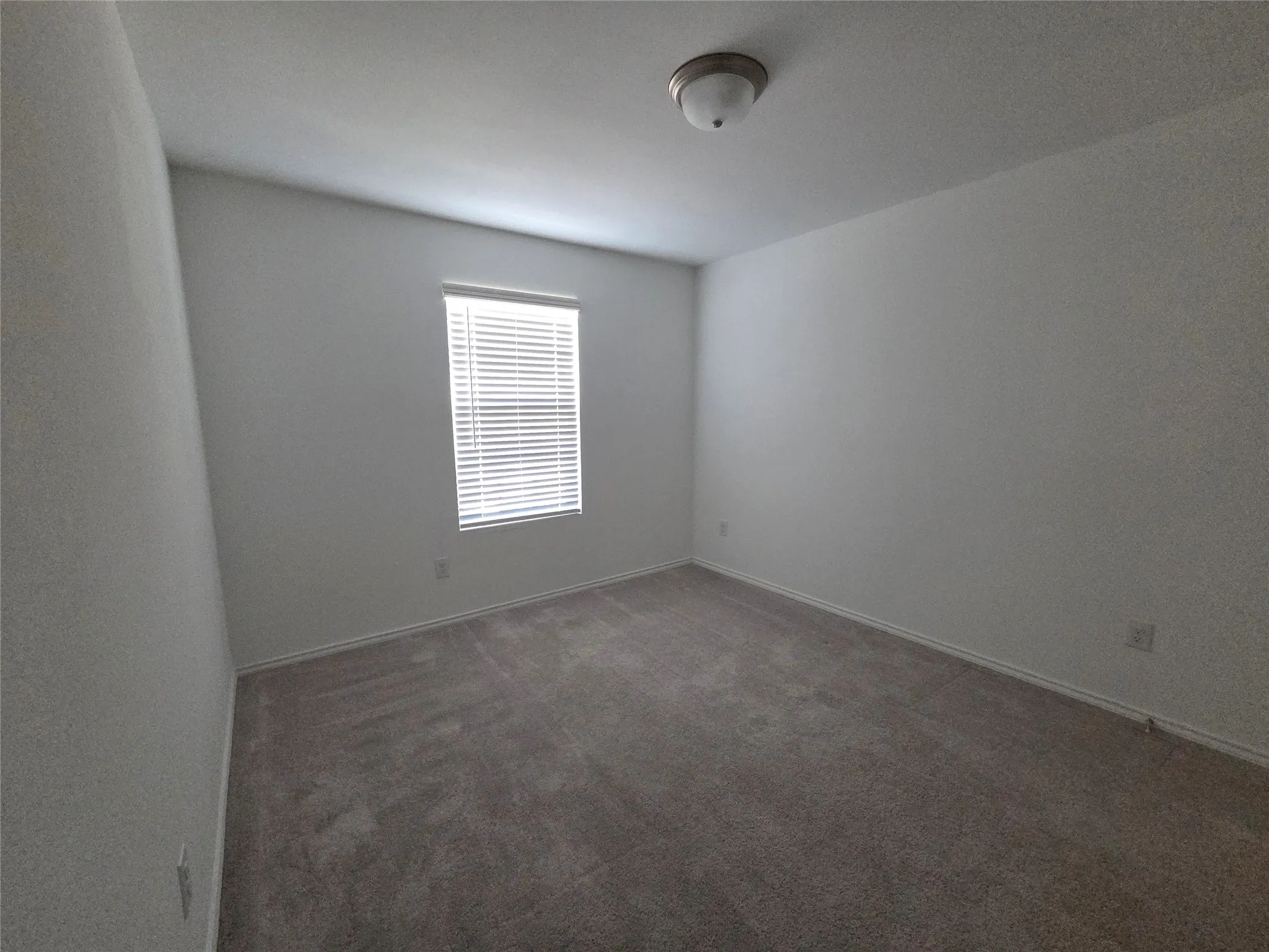 Neutral tone interior featuring a window with horizontal blinds, gray carpet, and a ceiling-mounted light fixture