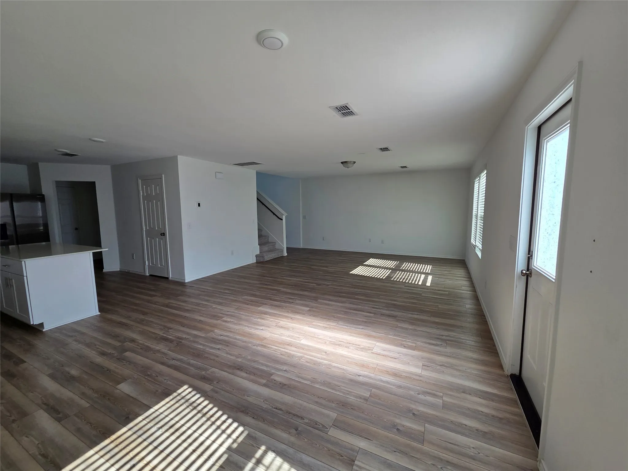 Open-concept living space featuring wood-finish flooring, white walls, and a kitchen island with white cabinetry