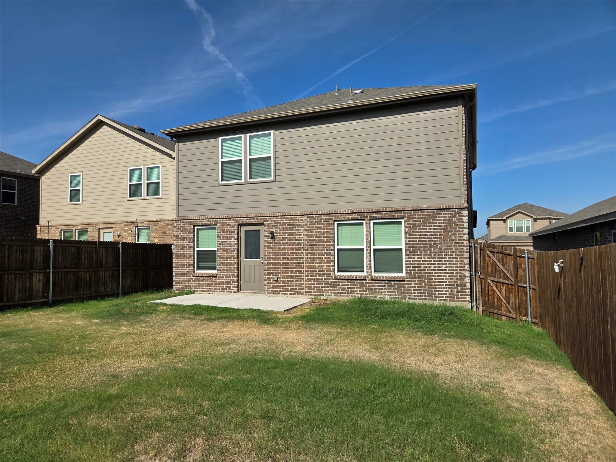Expansive backyard featuring a privacy fence, brick and siding exterior, multiple windows, and a concrete patio